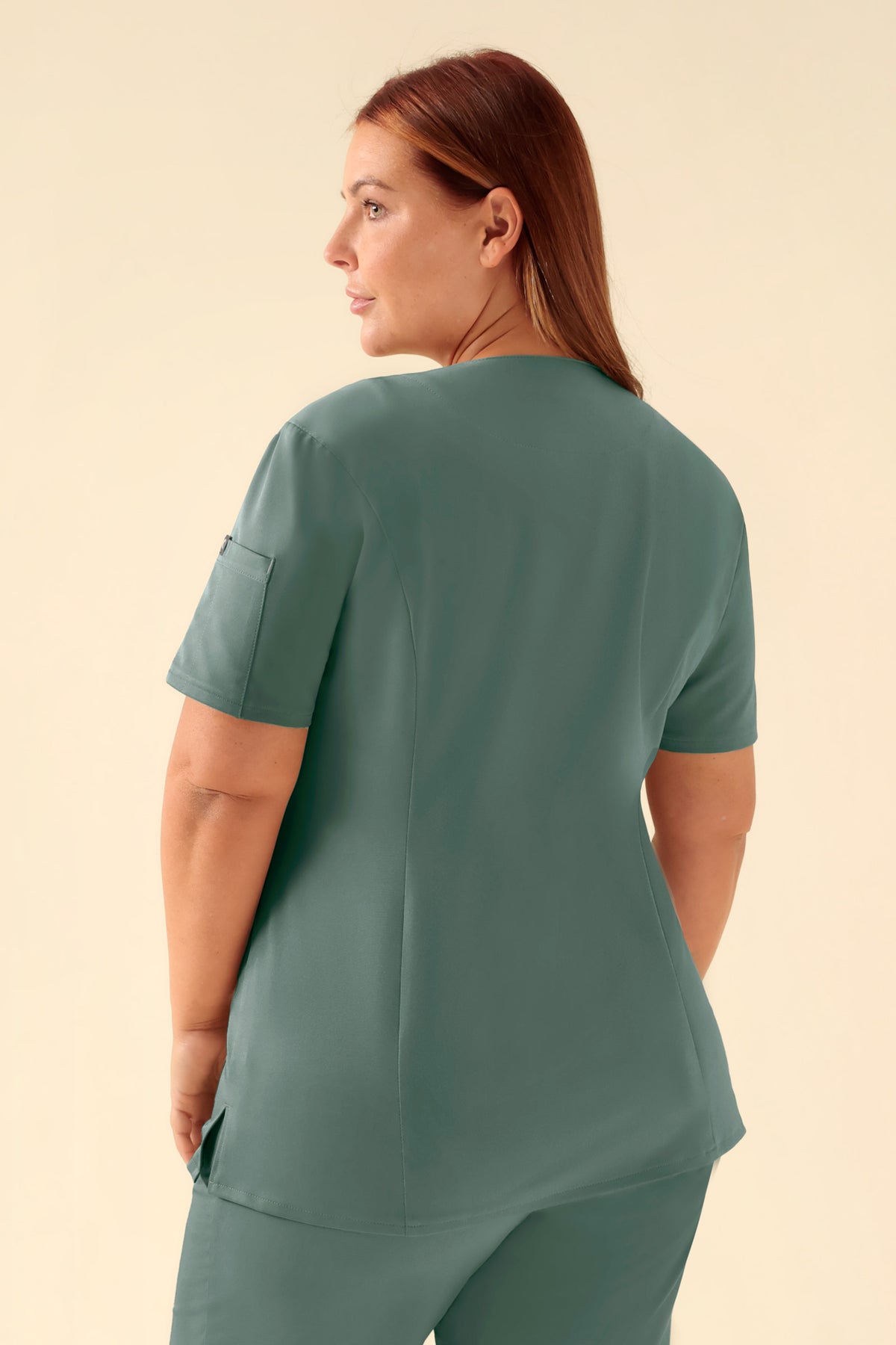 Rückansicht einer Person, die einen dunkelgrünen KAERE Kasack Damen – durchgeknöpft – trägt, mit V-Ausschnitt und einer Tasche am rechten Ärmel., Rückansicht Das Model ist 173 cm groß und trägt Größe XL
