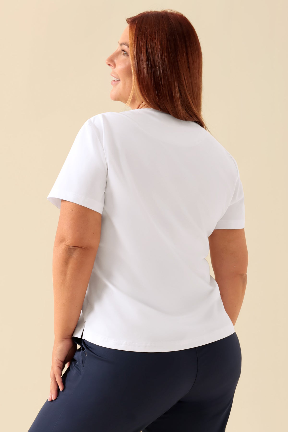 Eine Frau, von hinten gesehen, die ein weißes KAERE-Shirt für Damen – Rundhalsausschnitt, weiß – mit einer Brusttasche trägt., Rückansicht Das Model ist 173 cm groß und trägt Größe XL