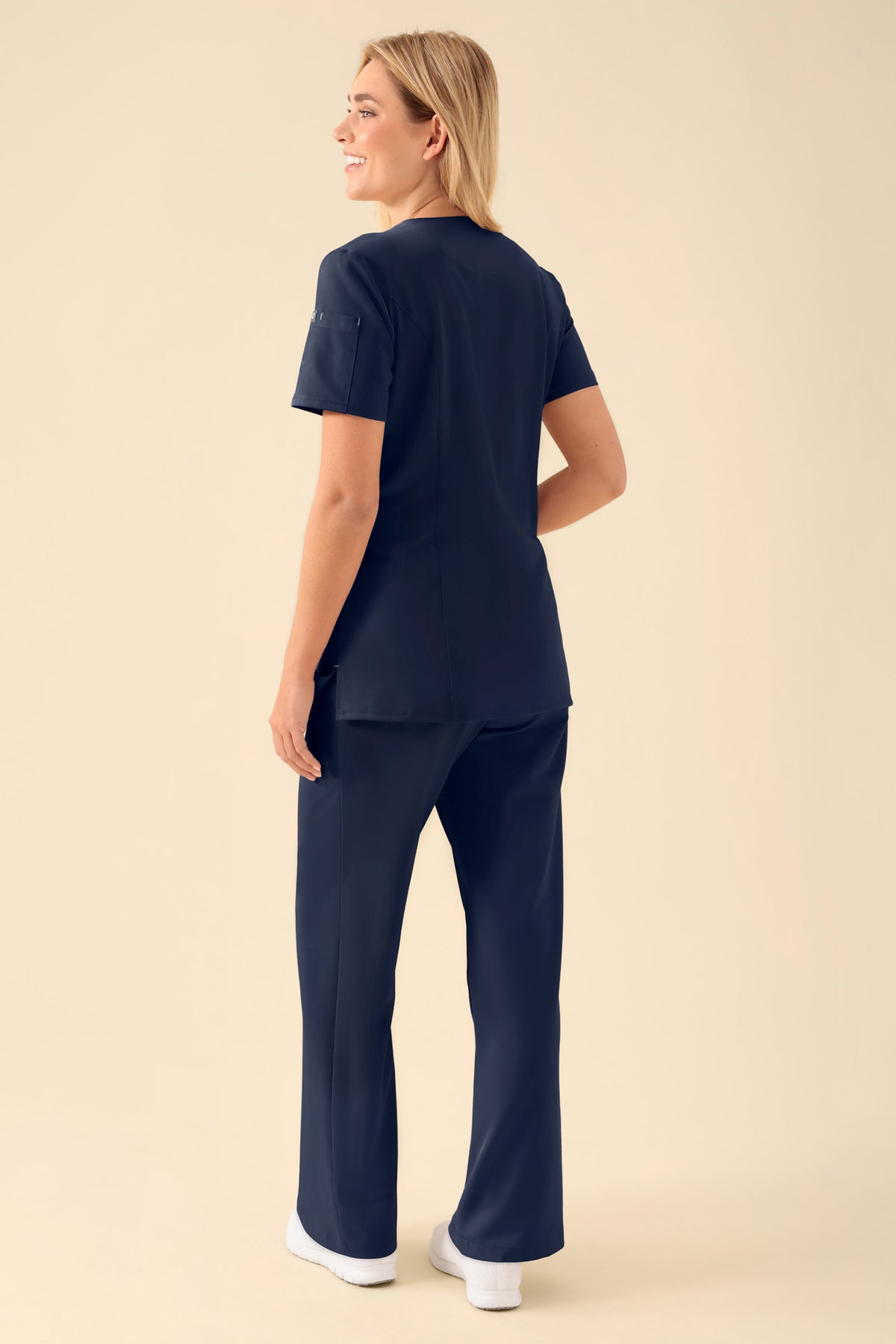 Eine Frau, die ein marineblaues KAERE Kasack Damen – durchgeknöpft navy Scrub-Oberteil mit V-Ausschnitt und eine dazu passende Hose mit Druckknopfleiste trägt.