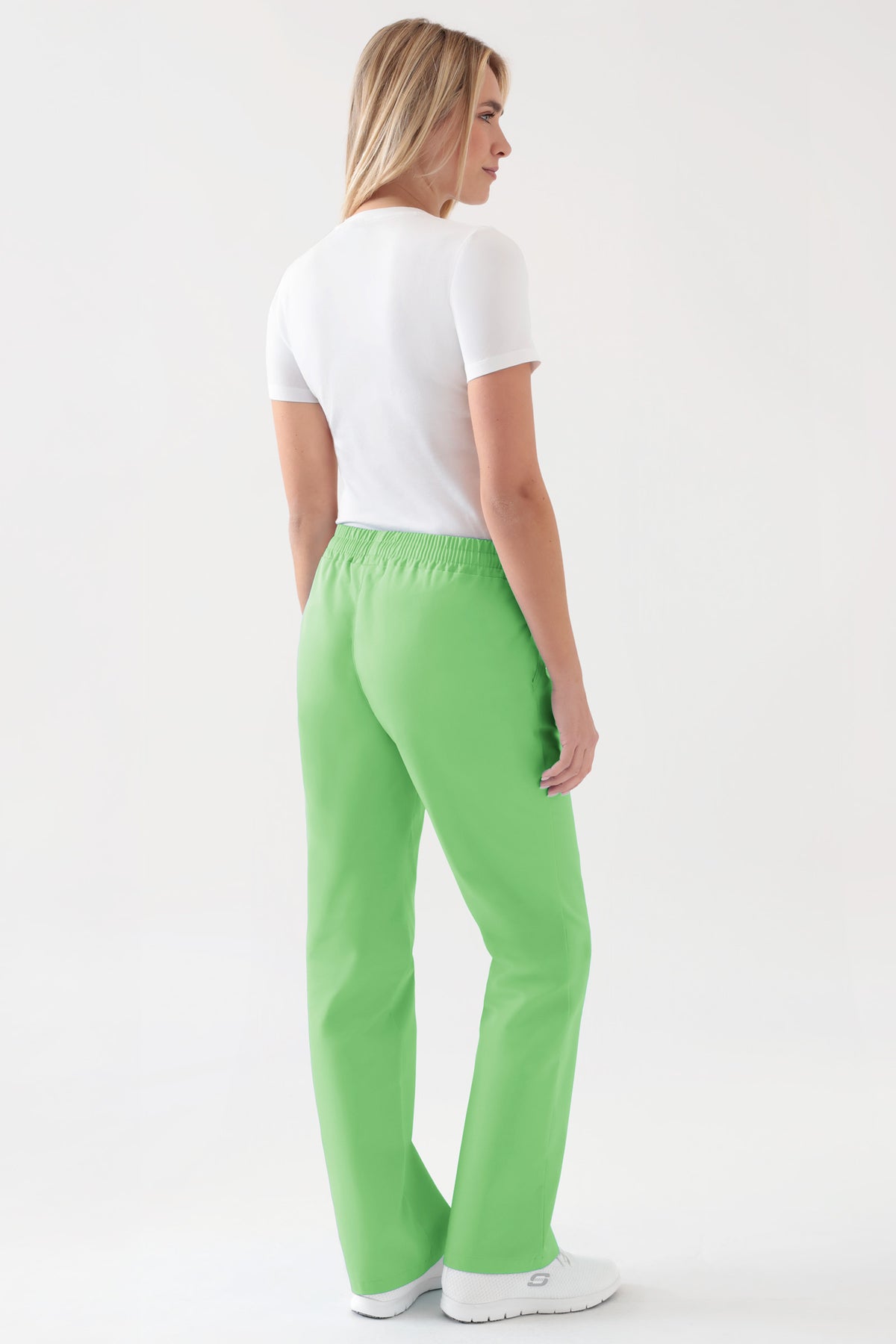 Rückansicht einer Frau, die ein weißes T-Shirt und eine Strumpfhose von CLINIC DRESS JUST STRONG für Damen – apfelgrün mit Gummizug und Seitentaschen – trägt.