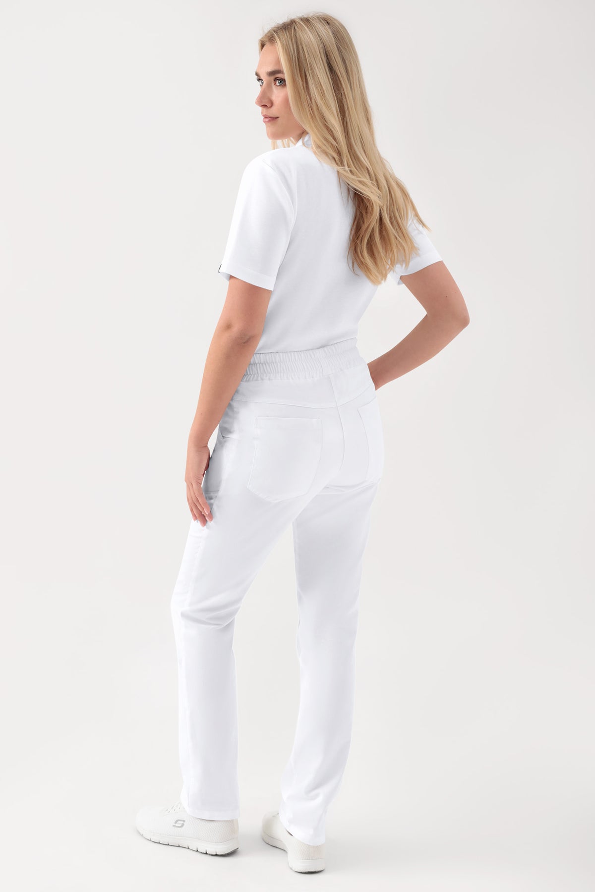 Eine Person, von hinten gesehen, die weiße GREEN Stretch Hose Unisex – Rundumgummibund weiß mit einem bequemen elastischen Bund und ein weißes kurzärmeliges Oberteil trägt.
