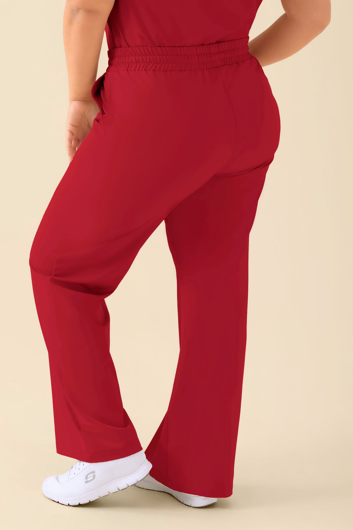 Eine Person, die eine rote, weit geschnittene KAERE Hose Damen mit bequemem elastischem Bund und weißen Sneakers trägt., Rückansicht