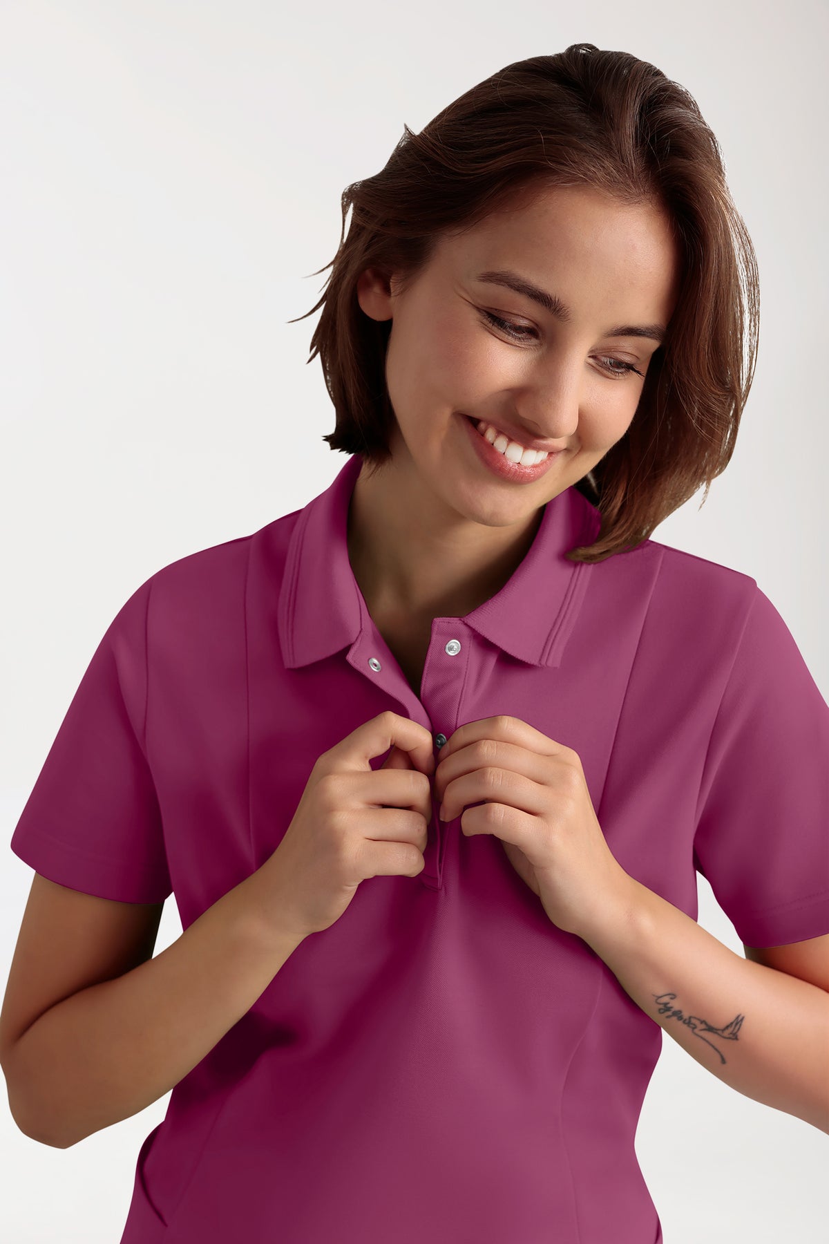Eine Frau, die lächelt, während sie die Knopfleiste eines beerenfarbenen COMFY FLEX Stretch Schlupfkasack Damen-Poloshirts zuknöpft.