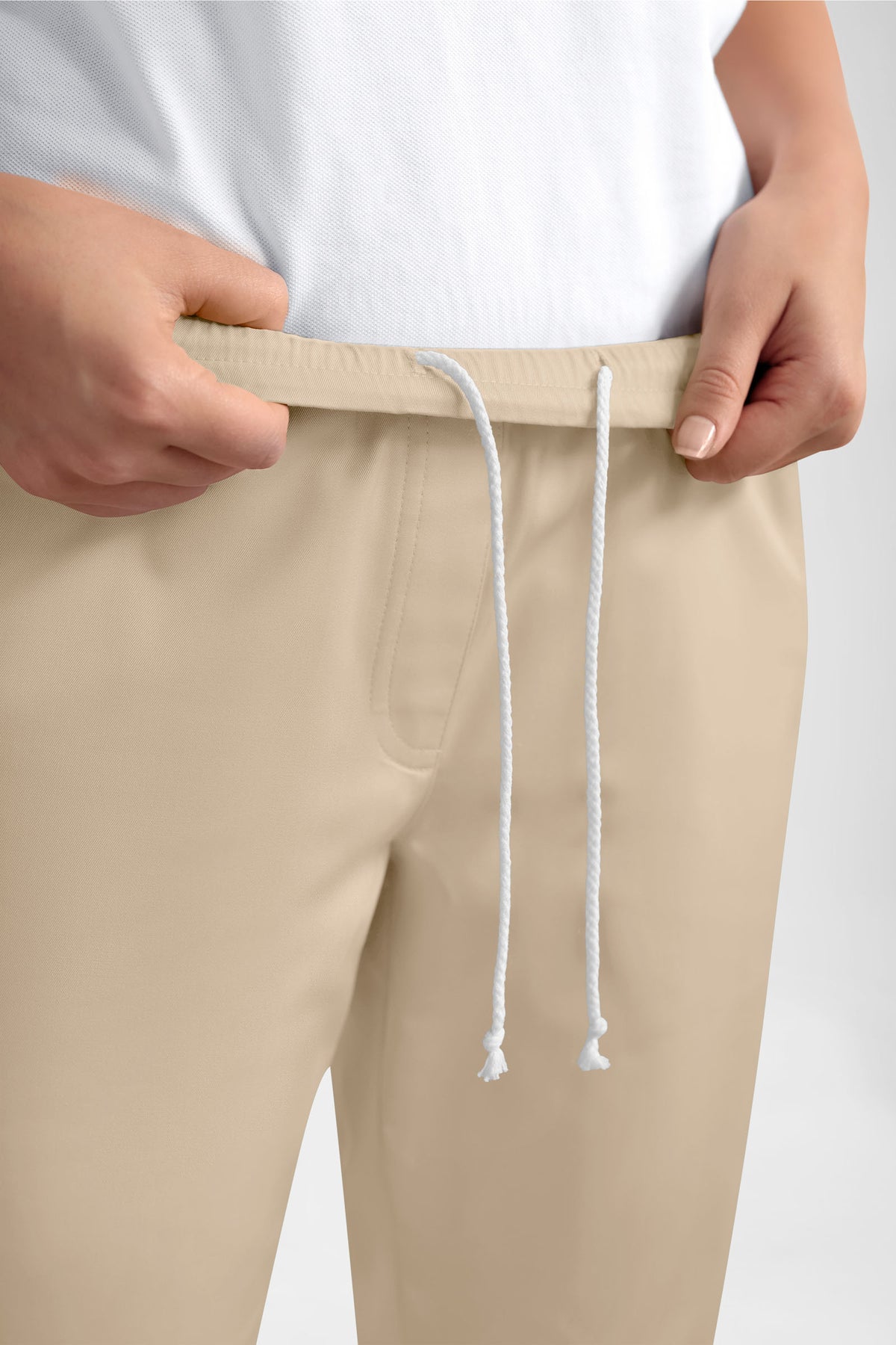 Eine Person, die eine sandfarbene GREEN Stretch-Hose für Damen im Jogginghosen-Stil trägt – mit Rundum-Gummibund, weißem Kordelzug und einer lässigen, lockeren Passform.
