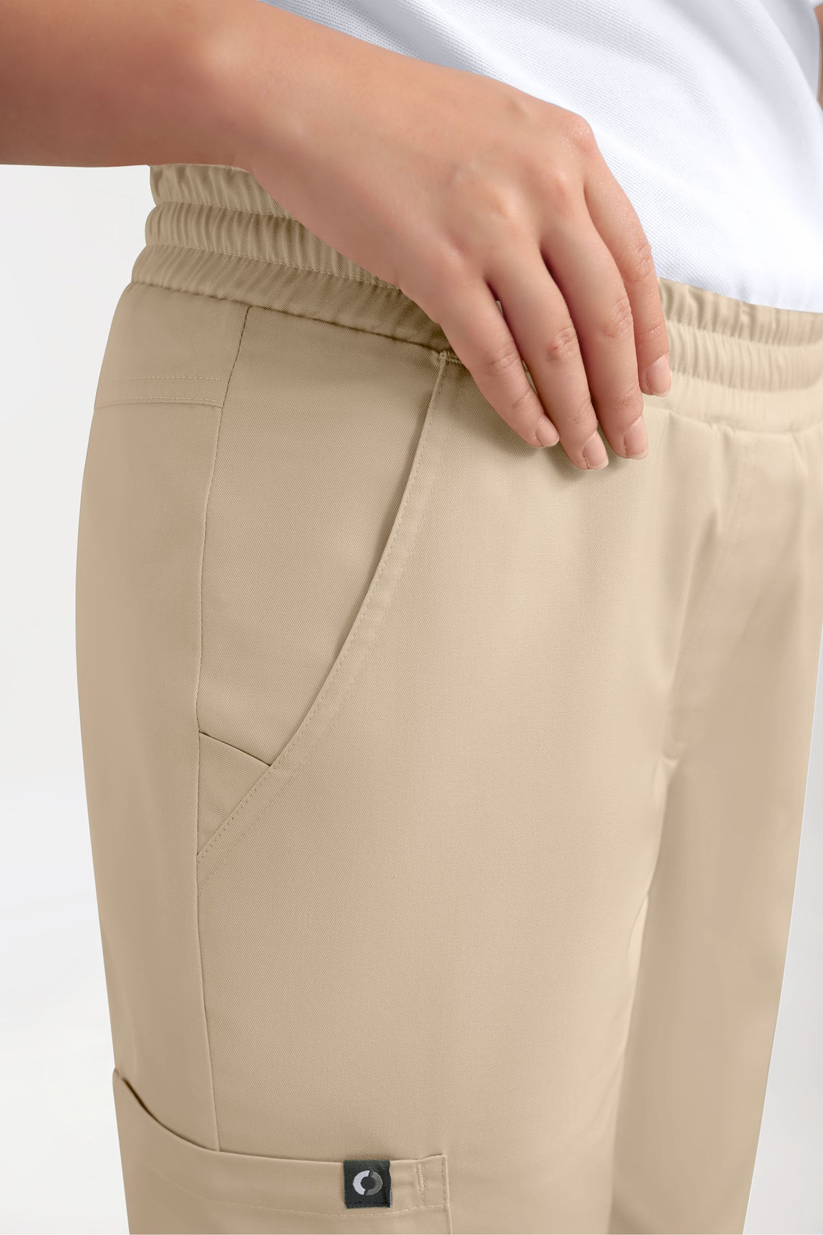 Nahaufnahme einer Person, die eine sandfarbene GREEN Stretch-Hose für Damen im Jogginghosen-Stil in der Farbe Sand mit Rundum-Gummibund und praktischen Seitentaschen trägt.