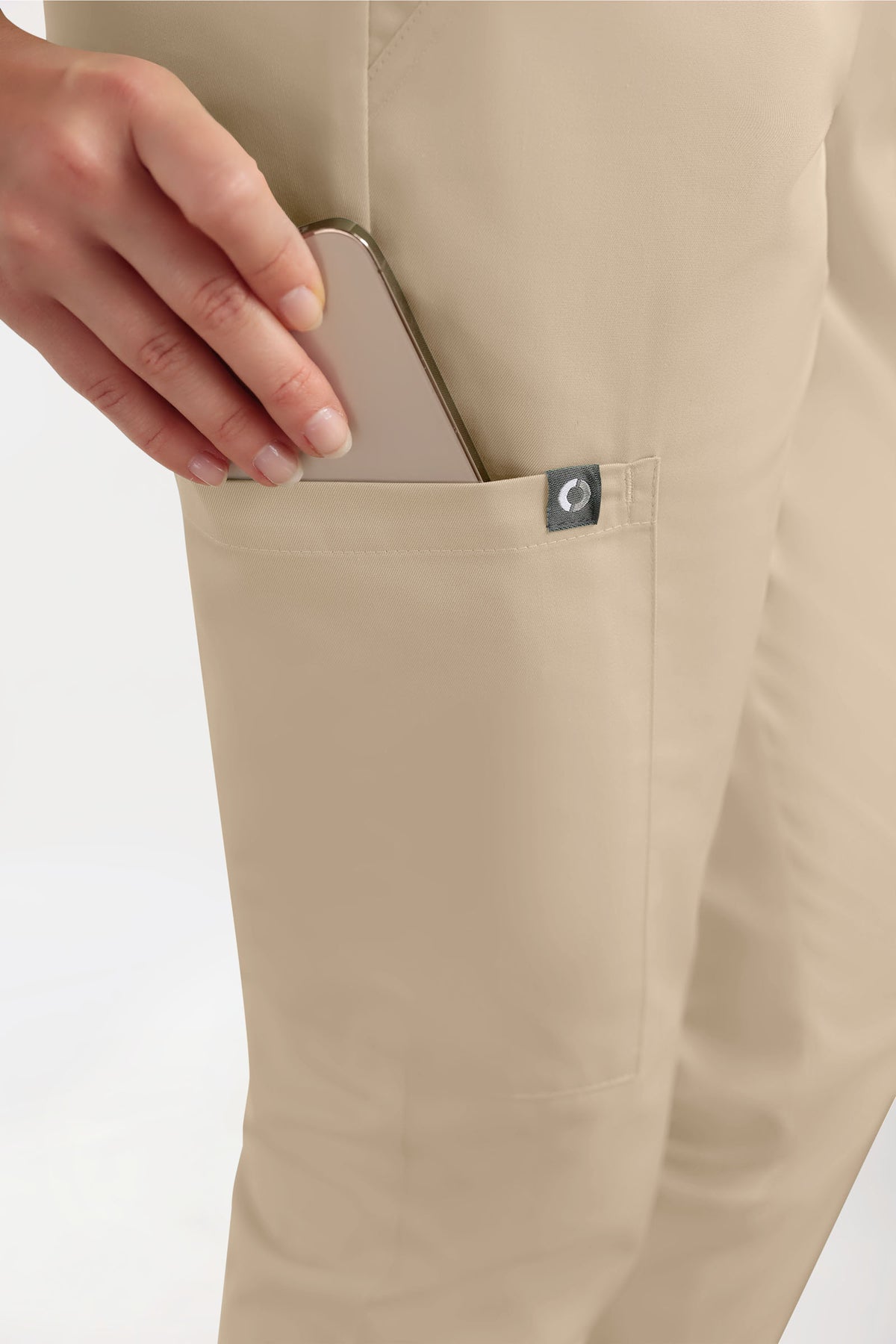 Eine Hand steckt ein Smartphone in die Seitentasche einer sandfarbenen GREEN Stretch Hose Damen – im Jogginghosen-Stil mit lässiger Passform.