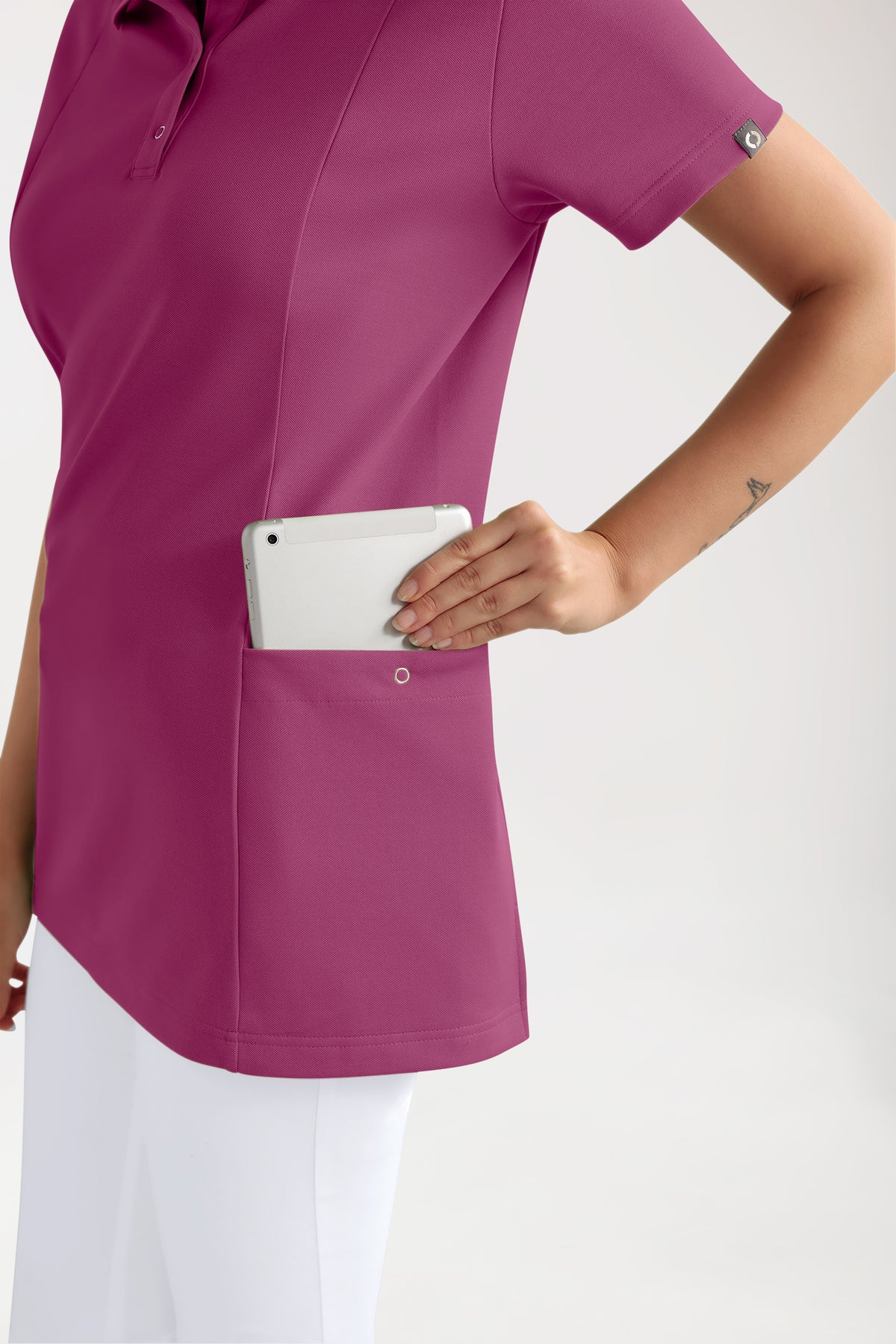 Eine Person, die einen COMFY FLEX Stretch Schlupfkasack für Damen – Polokragen in der Farbe Berry trägt und ein kleines Tablet aus einer großen Seitentasche herausholt.