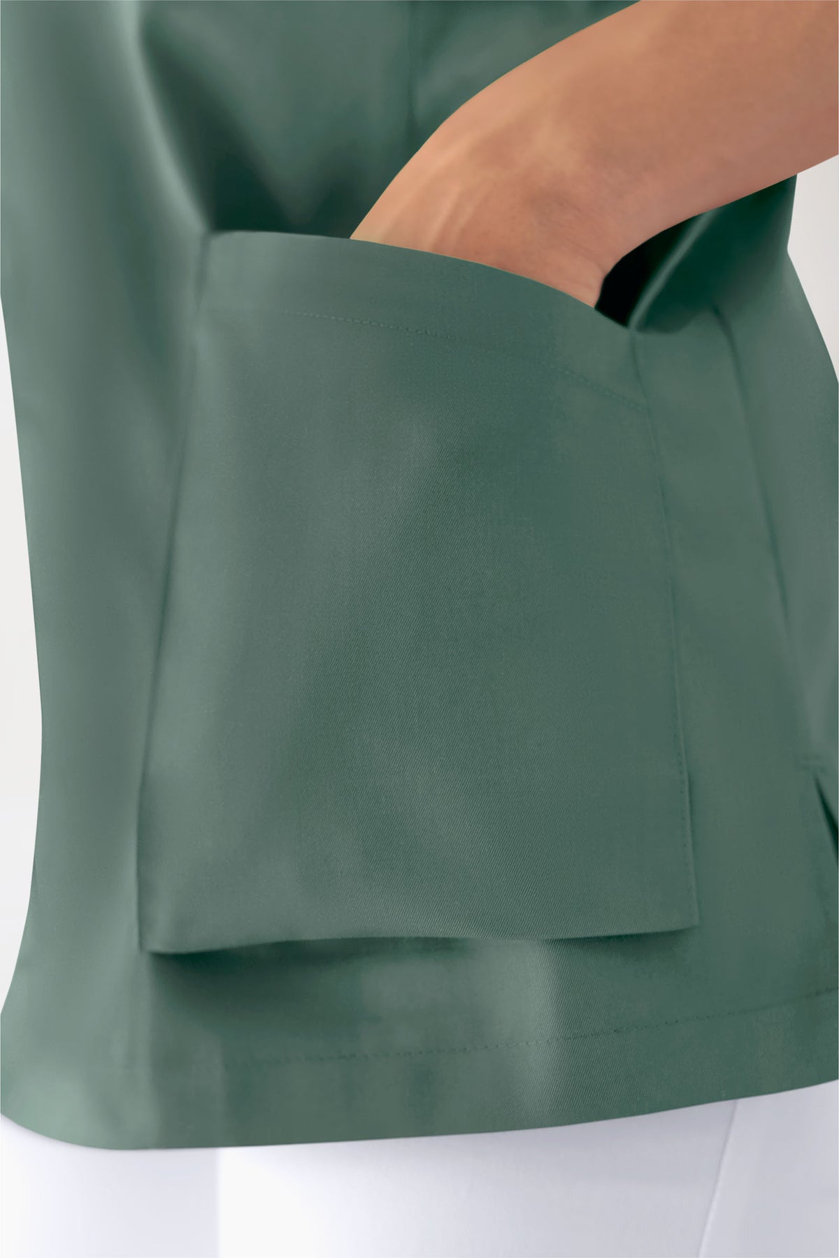 Eine Hand greift in die große Vordertasche eines dunkelgrünen CORE Schlupfkasack Damen – V-Ausschnitt dunkelgrün mit Raglanärmeln.