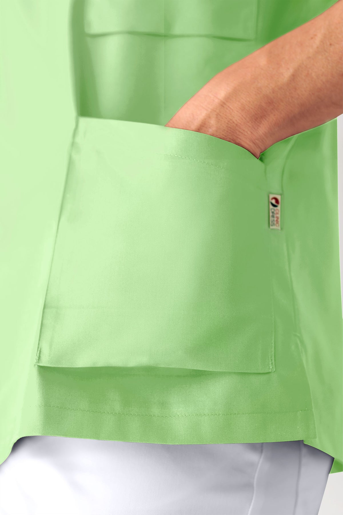 Eine Hand greift in die Brusttasche eines hellgrünen CORE Kasack Herren – durchgeknöpft, apfelgrün, mit V-Ausschnitt.