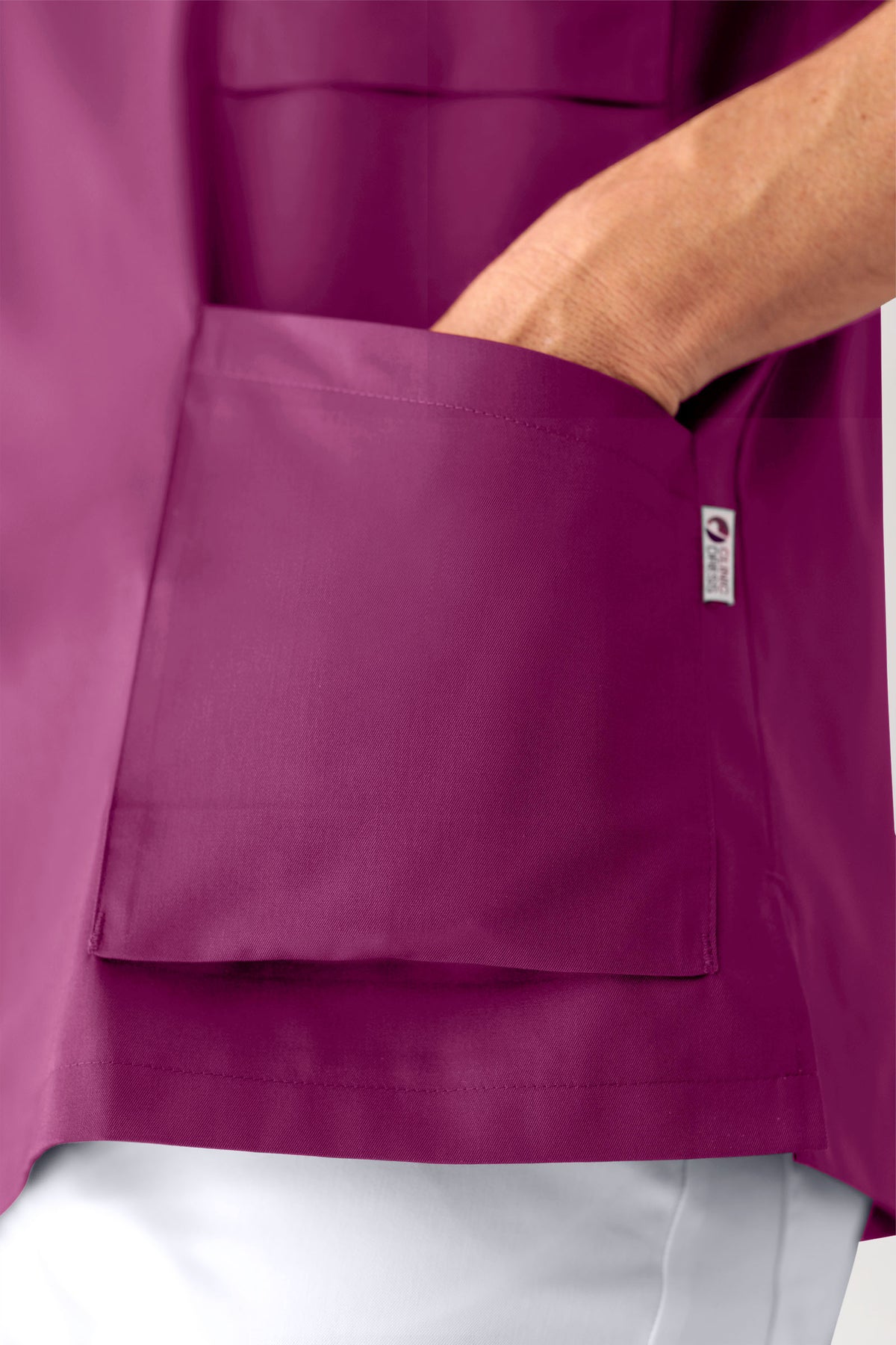 Eine Hand steckt in der großen aufgesetzten Tasche eines beerenfarbenen CORE Schlupfkasack Herren – V-Ausschnitt-Kitteloberteils.