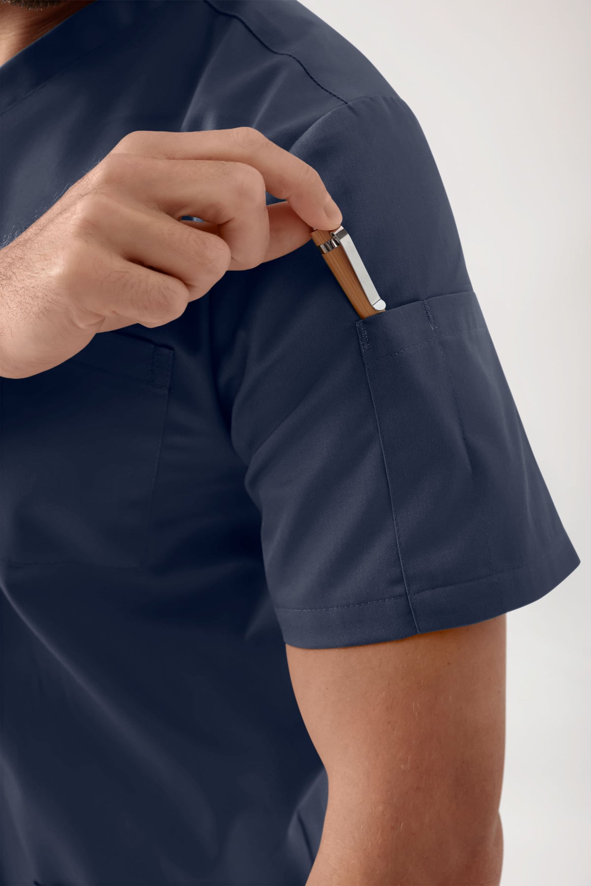 Nahaufnahme einer Person, die einen Stift in die Tasche eines marineblauen GREEN Stretch Schlupfkasack Herren – V-Ausschnitt in Marineblau (medizinisches Oberteil) steckt.