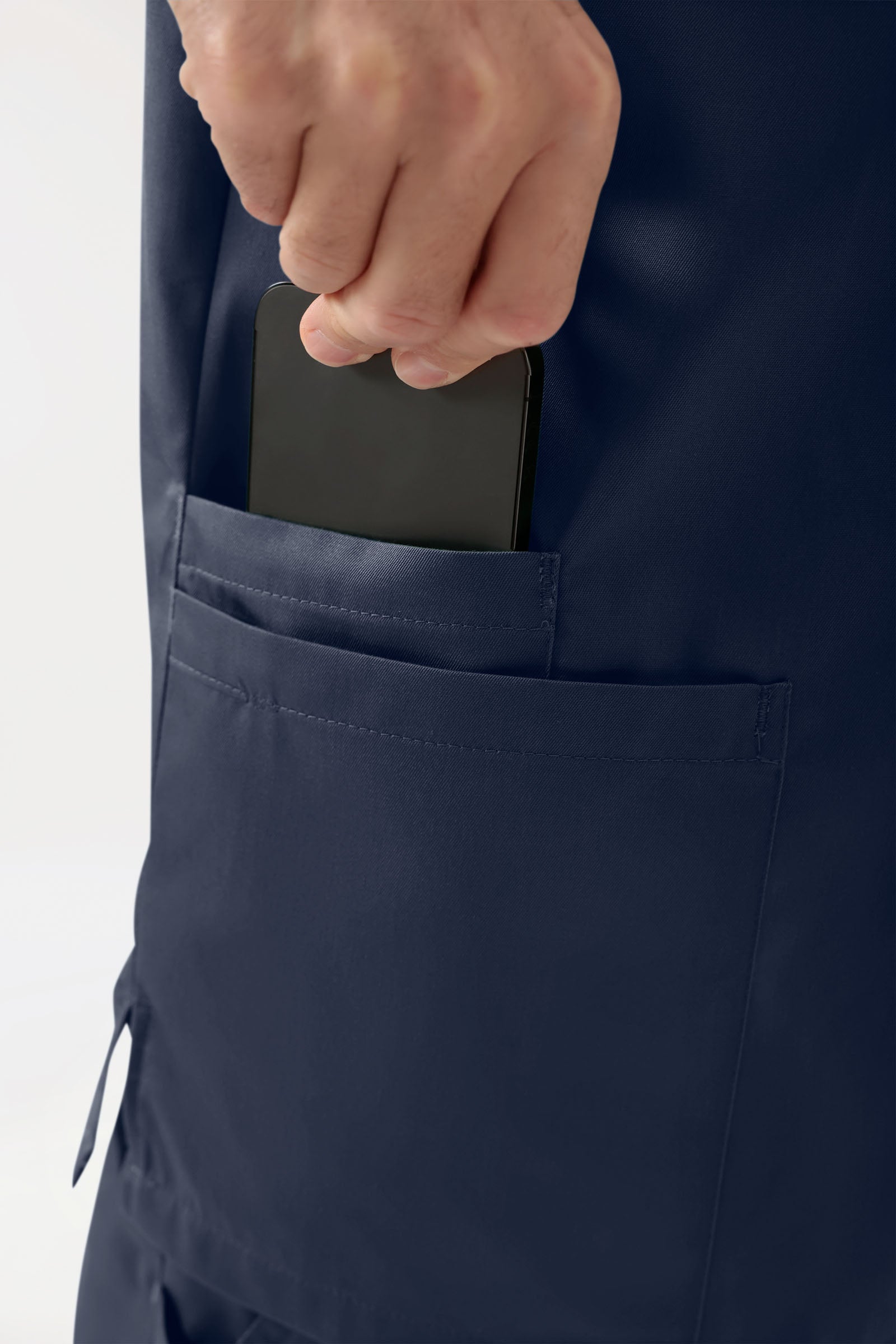 Eine Hand, die ein Smartphone in eine Seitentasche eines marineblauen GREEN Stretch Schlupfkasack Herren – V-Ausschnitt in Marineblau steckt.