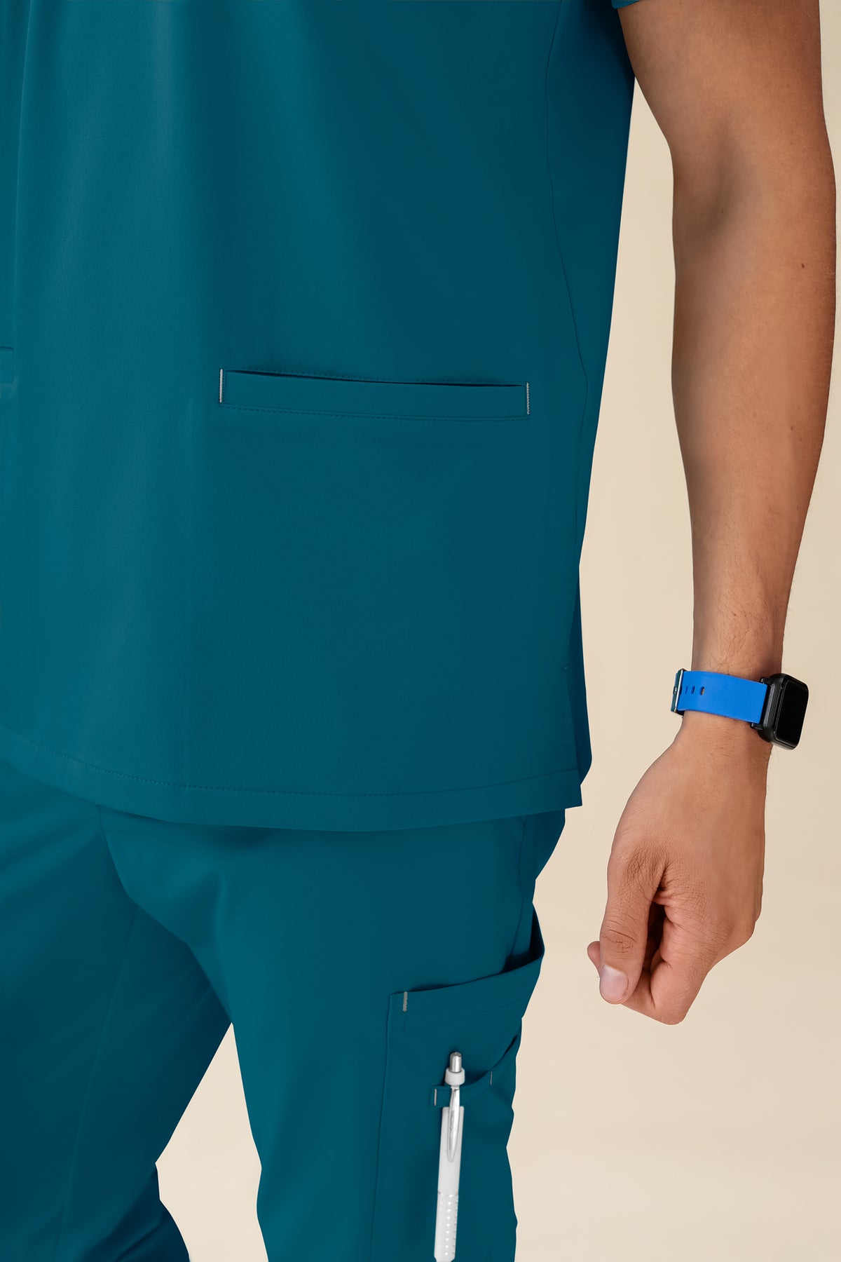 KAERE Herren-Schlupfjacke – Scrub-Oberteil mit V-Ausschnitt in der Farbe Petrol und einer Brusttasche sowie dazu passende Scrub-Hose mit einer Seitentasche für einen Stift.