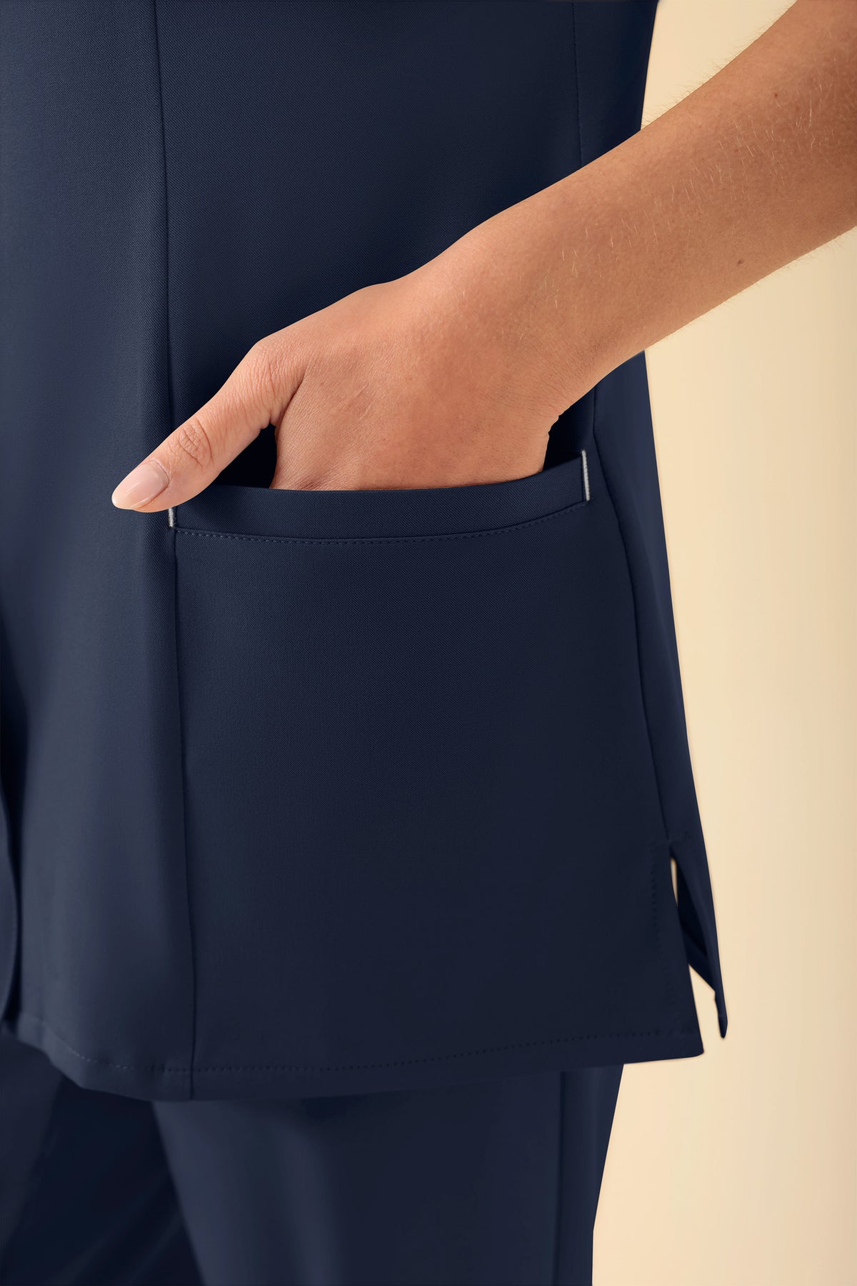 Eine Hand ruht in der Seitentasche eines marineblauen KAERE Kasack Damen - durchgeknöpft navy Scrub-Oberteils mit V-Ausschnitt.