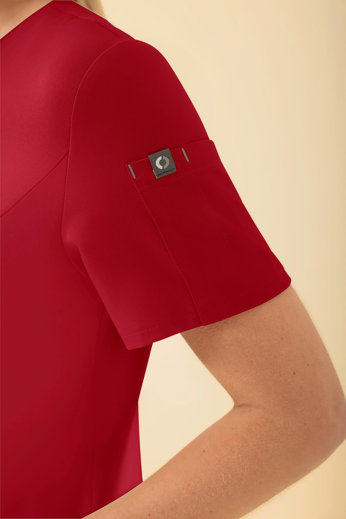 Nahaufnahme eines roten KAERE Kasack Damen – durchgeknotetes rotes OP-Oberteil mit V-Ausschnitt und einem kleinen grauen Logo-Etikett am linken Ärmel.