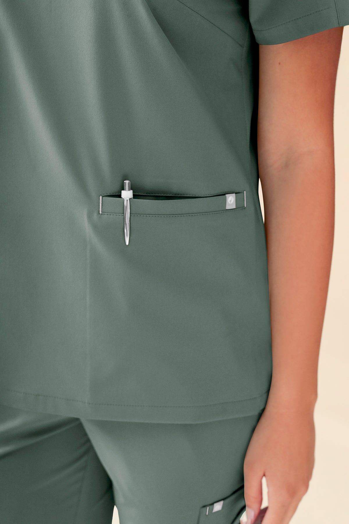 Nahaufnahme eines dunkelgrünen KAERE Schlupfkasacks für Damen – Scrub-Top mit V-Ausschnitt in Dunkelgrün, mit einer Brusttasche, in der ein Stift steckt.