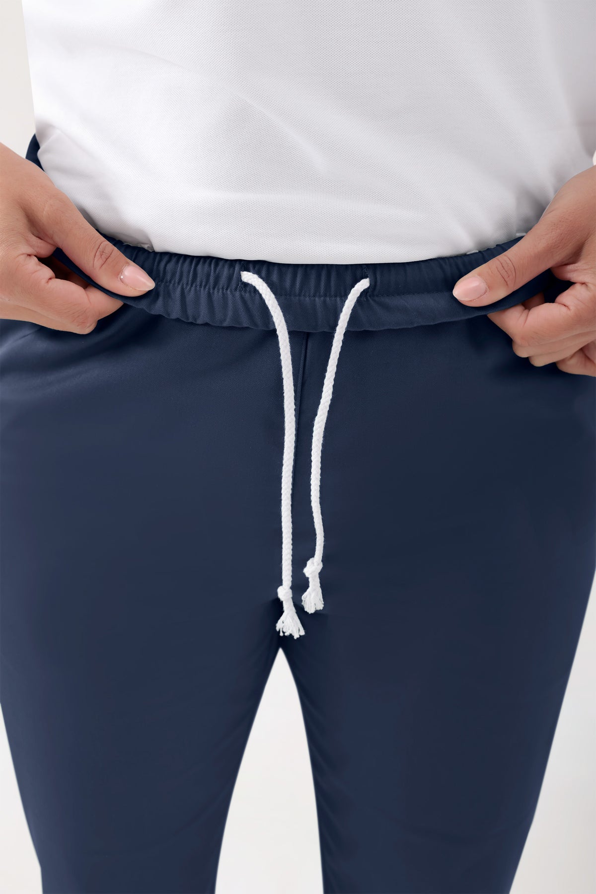 Hände, die die marineblaue GREEN Stretch-Strumpfhose Unisex – Rundumgummibund am elastischen Kordelzugbund festhalten und dabei die lässige Beinweite zeigen.