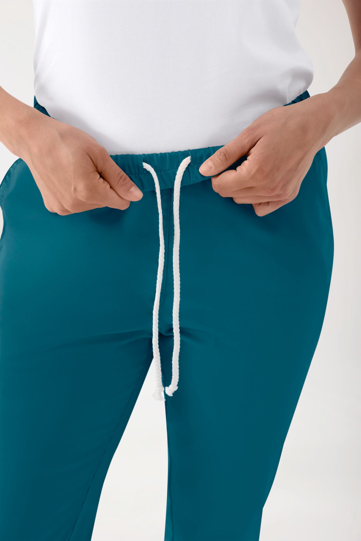 Eine Person, die eine Stretch Hose Unisex – Rundumgummibund in der Farbe Petrol trägt, eine OP-Hose in der Farbe Teal mit einem bequemen elastischen Bund, einer lockeren Passform an den Beinen und einem weißen Kordelzug.