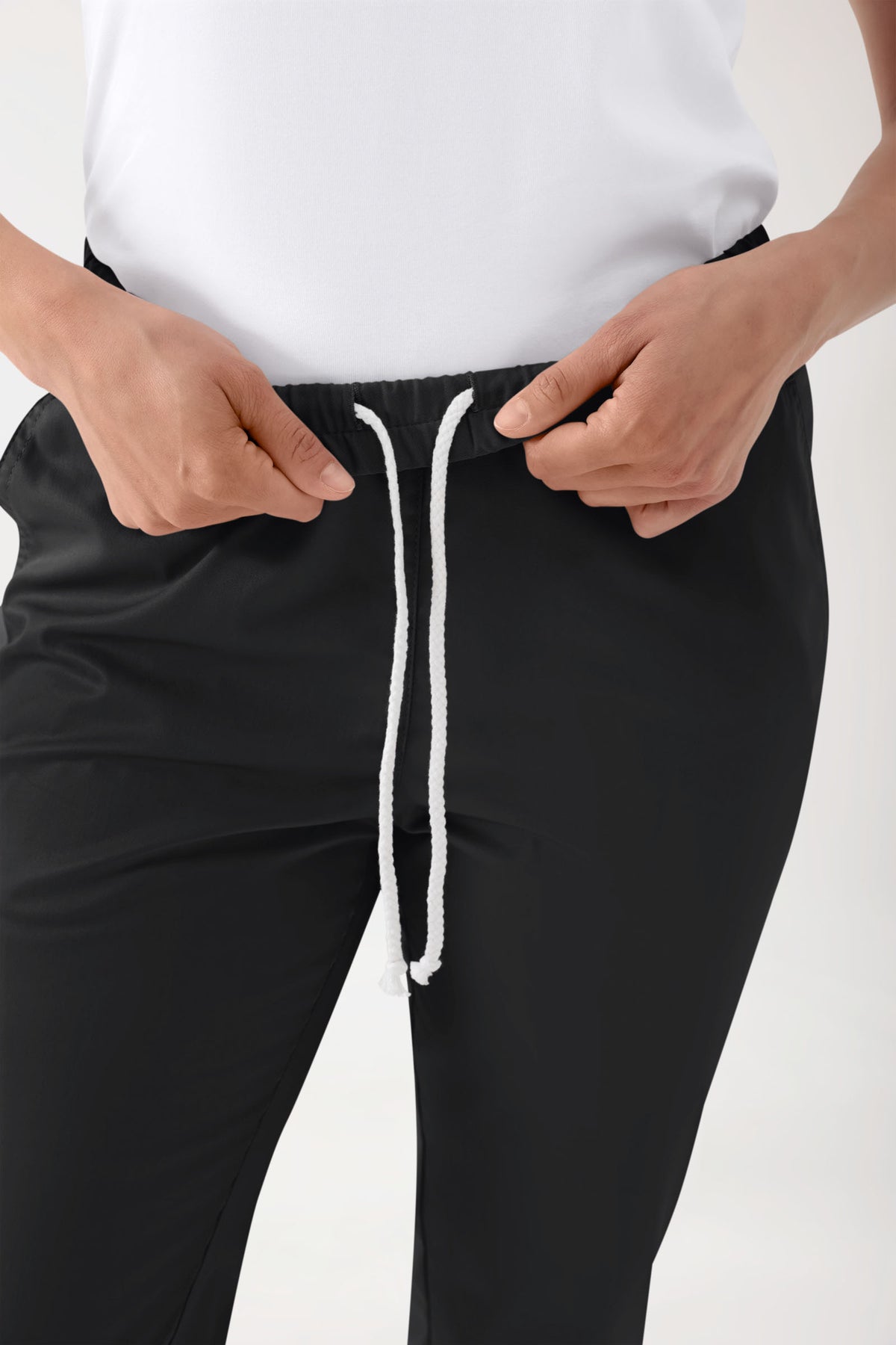 Nahaufnahme von Händen, die den weißen Kordelzug an einer schwarzen Stretch-Strumpfhose Unisex – Rundumgummibund schwarz mit bequemem elastischem Bund und lässiger Beinweite – verstellen.