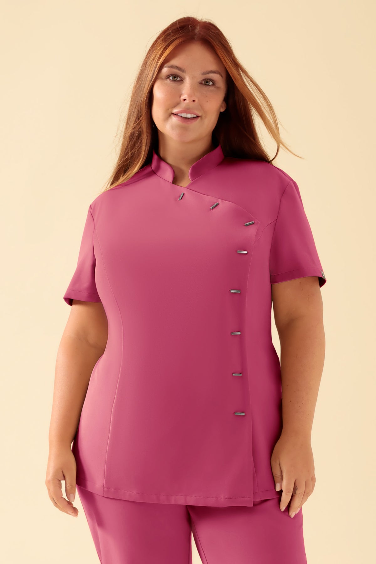 Ein rosafarbener KAERE-Kasack für Damen mit Stehkragen, kurzen Ärmeln und einer asymmetrischen Knopfleiste., Vorderansicht Das Model ist 173 cm groß und trägt Größe XL
