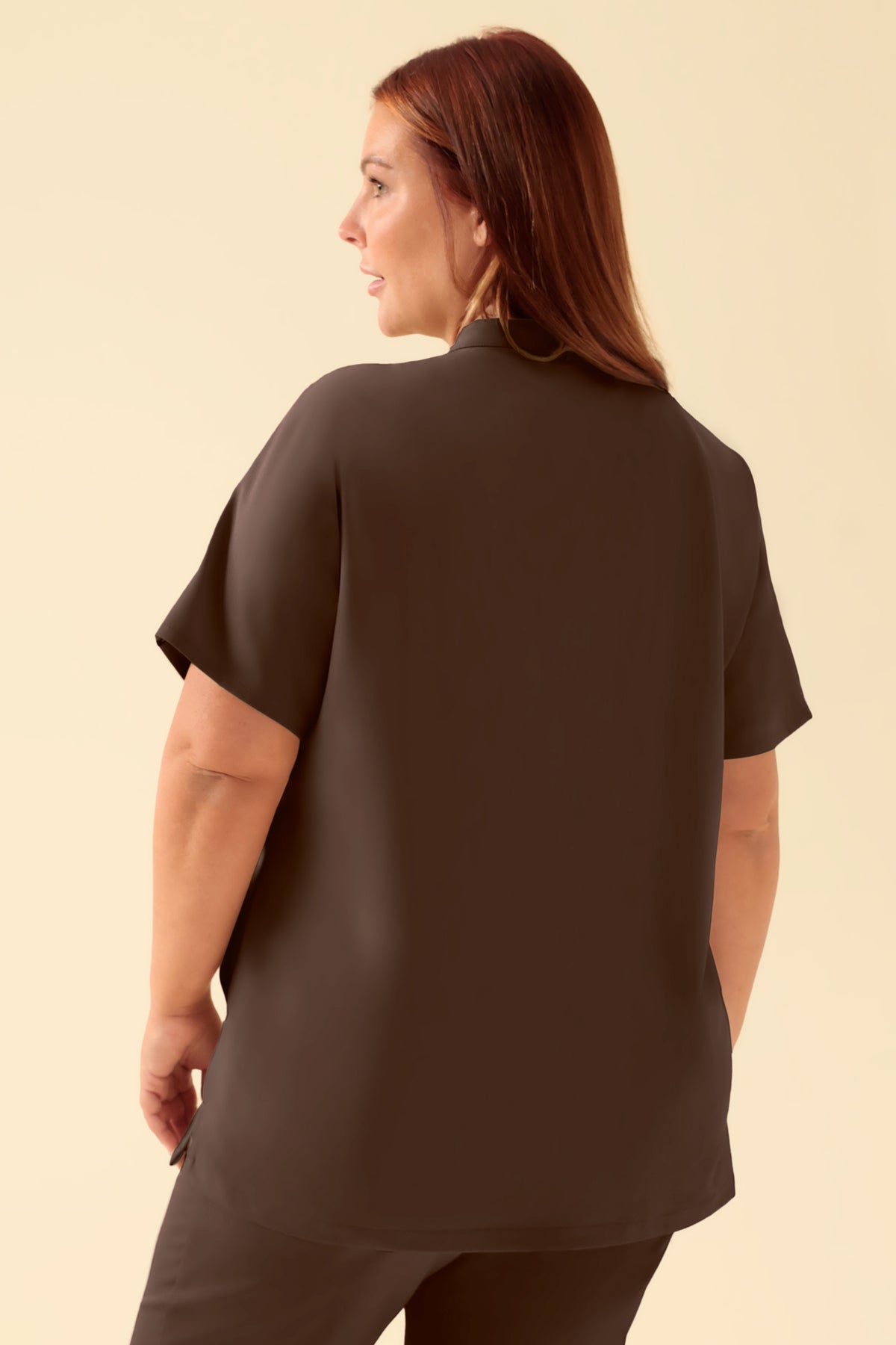 Rückansicht einer Frau, die einen kaffeefarbenen KAERE Schlupfkasack für Damen mit Stehkragen, kurzen Ärmeln und Seitentaschen trägt., Vorderansicht Das Model ist 173 cm groß und trägt Größe XL