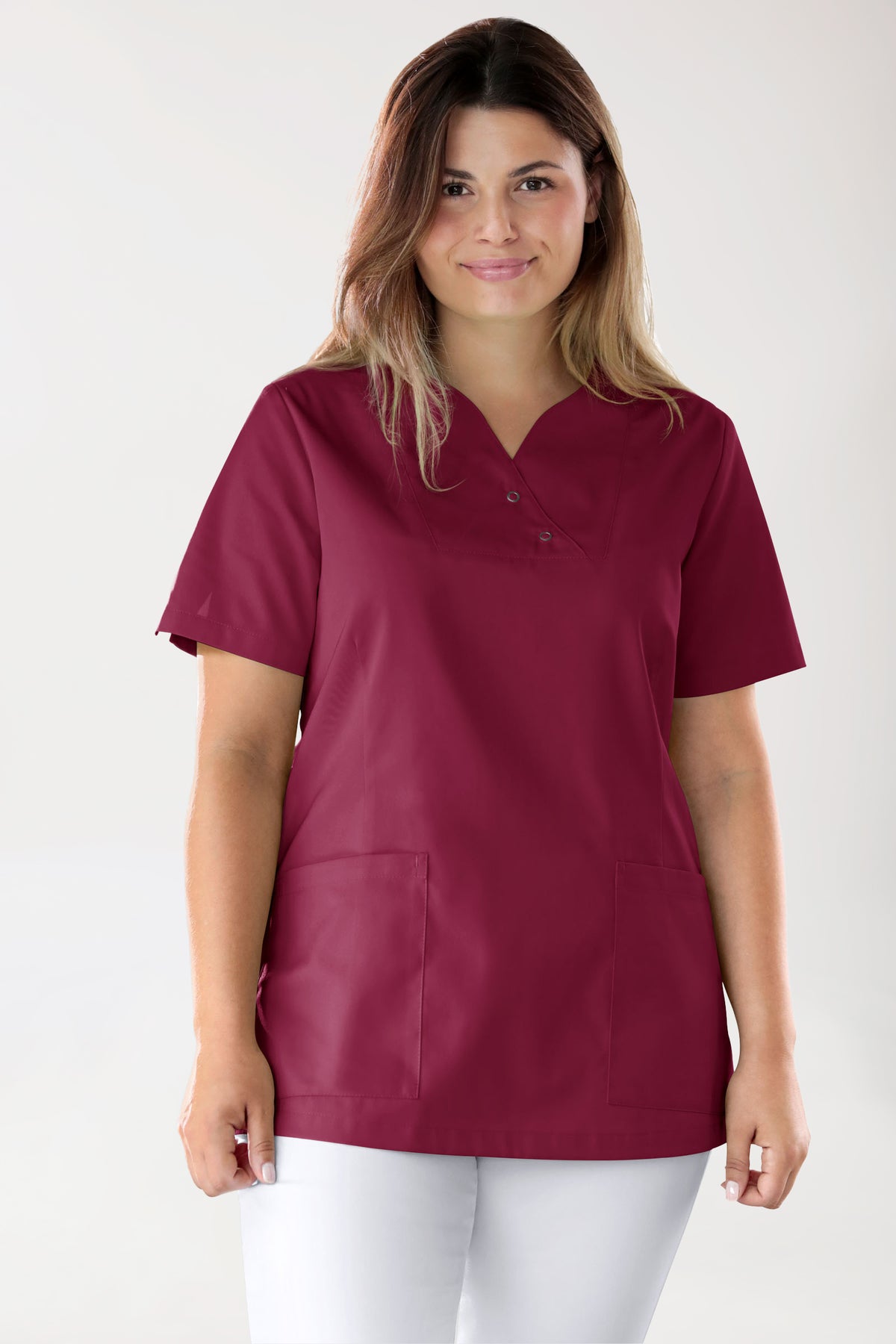 Eine Frau, die einen bordeauxfarbenen CORE Schlupfkasack für Damen in Curved-Fit – mit Druckknöpfen und kurzen Ärmeln sowie Druckknopfdetails – über einer weißen Hose trägt.