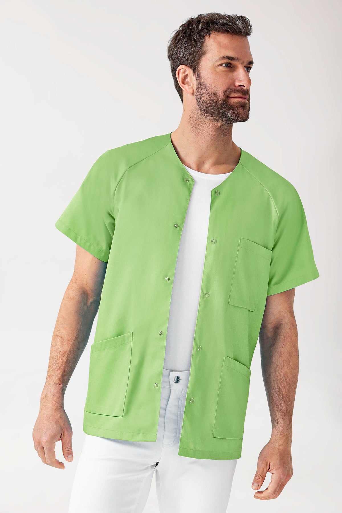 Ein Mann, der ein CORE Kasack Herren – durchgeknöpftes, apfelgrünes Scrub-Oberteil mit V-Ausschnitt und Raglanärmeln über einem weißen T-Shirt trägt.
