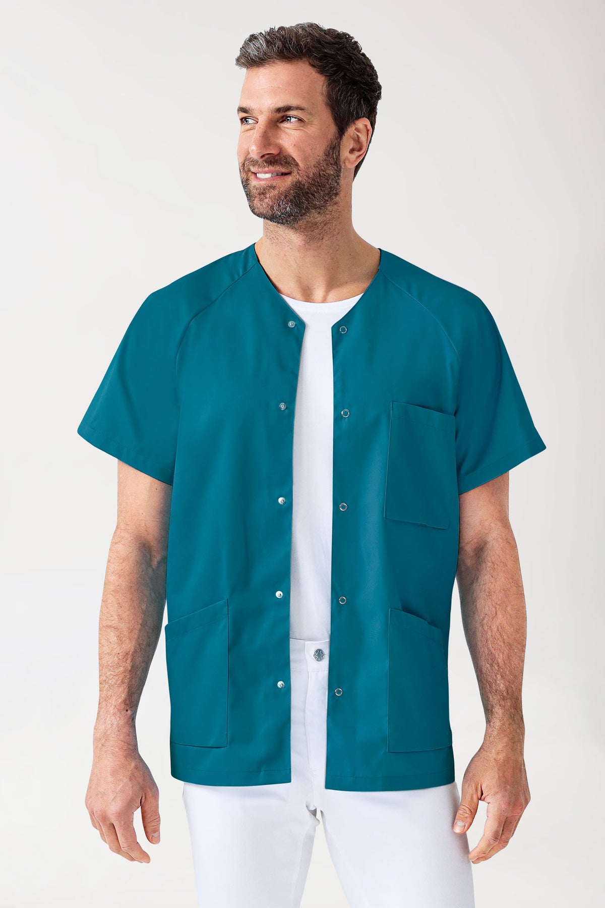 Ein Mann, der eine petrolfarbene CORE Kasack Herren – durchgeknöpft-Tunika mit Raglanärmeln und Druckknopfverschlüssen über einem weißen T-Shirt und einer Hose trägt.