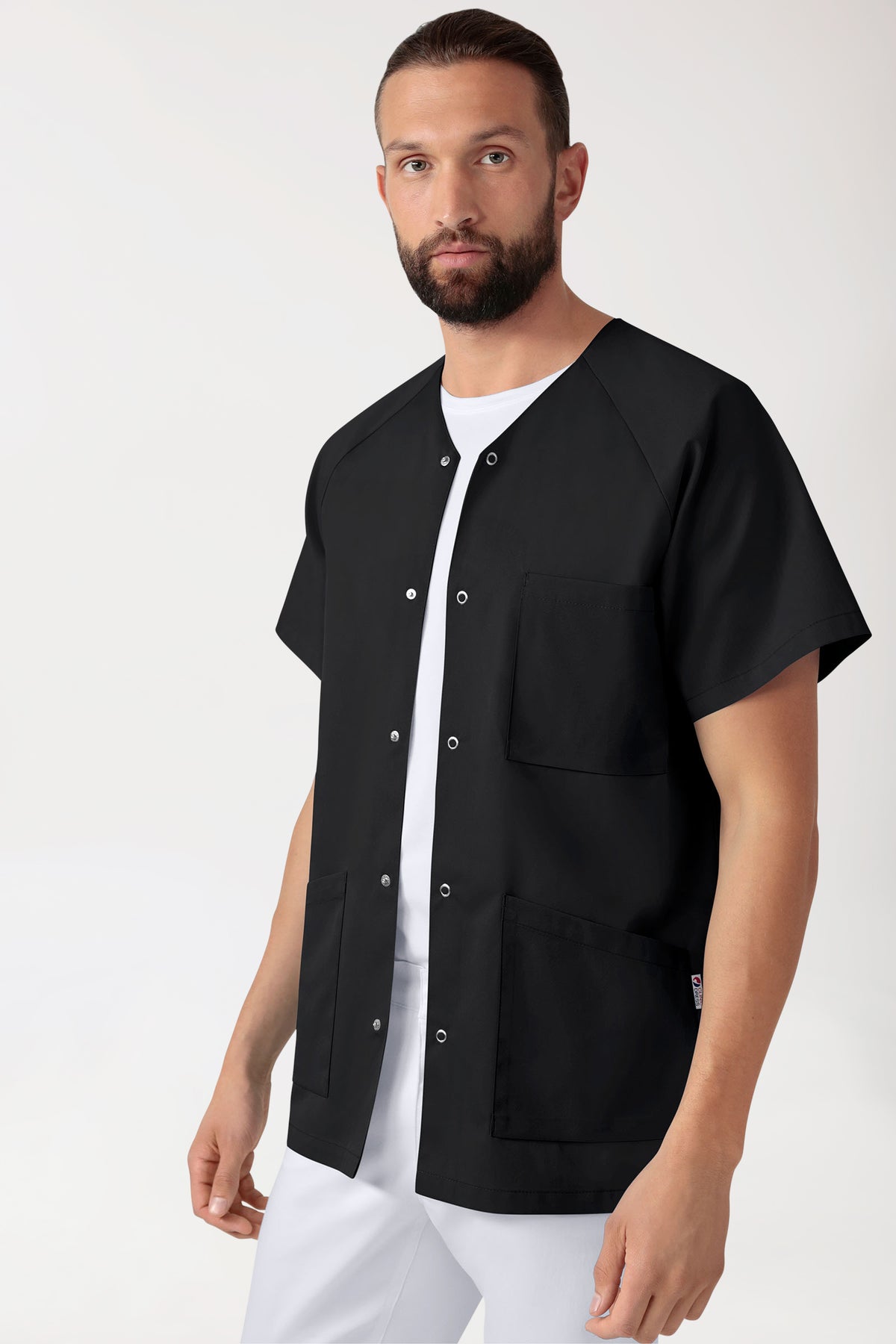 Ein Mann trägt eine schwarze CORE Kasack Herren – durchgeknöpft schwarz Tunika mit V-Ausschnitt und Brusttasche über einem weißen T-Shirt und einer weißen Hose.
