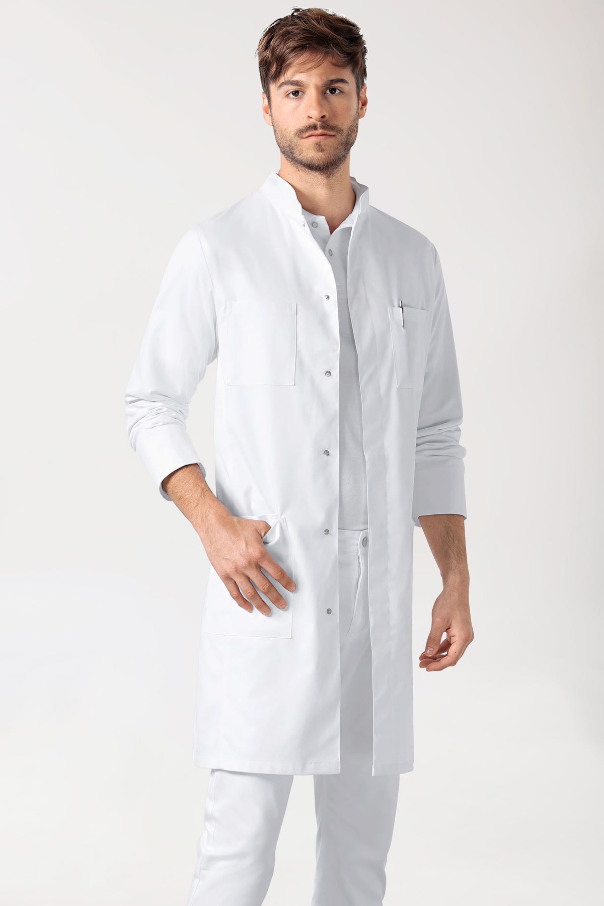 Ein Mann, der einen weißen CLINIC DRESS Mantel Herren – Druckknopfleiste – Stehkragen weiß trägt, einen langärmeligen Laborkittel mit Stehkragen und verdeckter Druckknopfleiste.