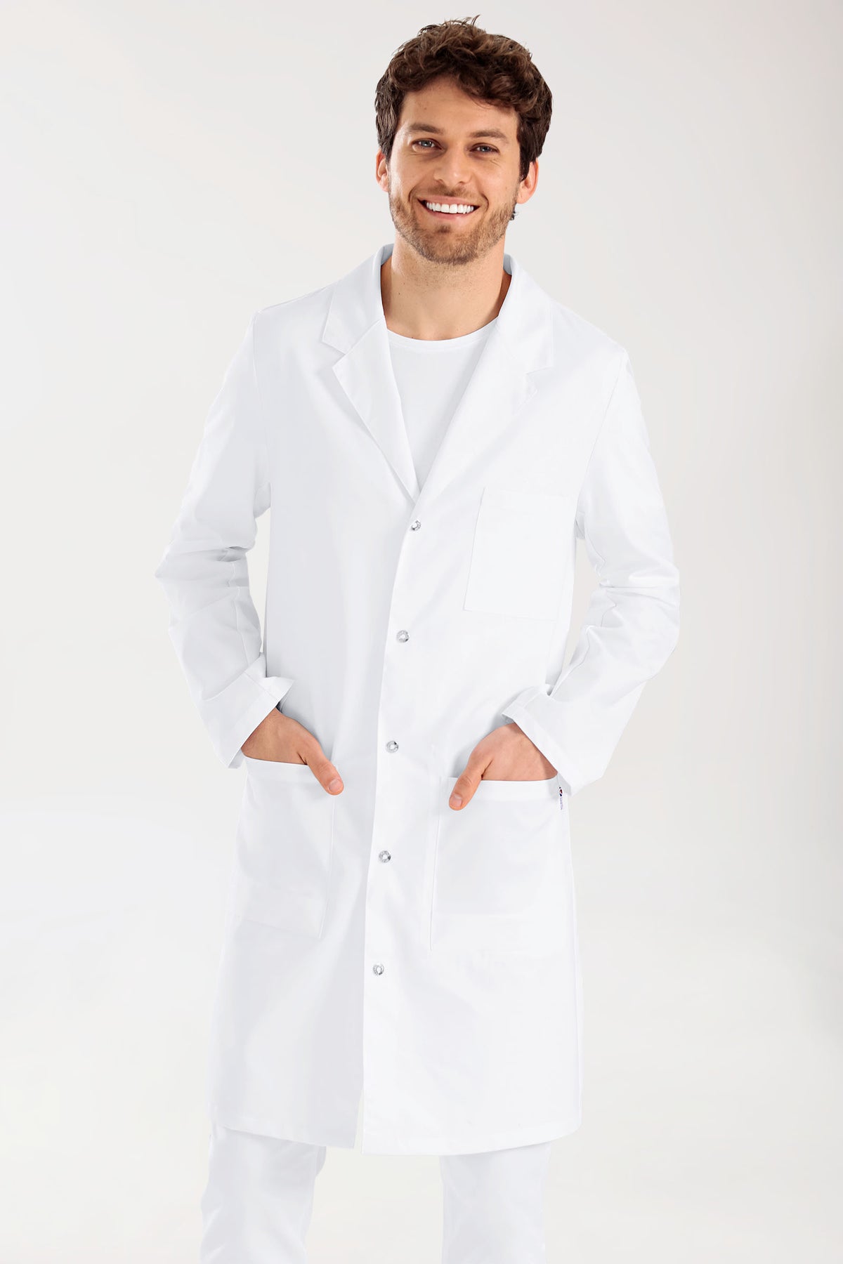 Ein lächelnder Mann trägt einen weißen Kittel CLINIC DRESS Mantel Herren – Reverskragen – Druckknopfleiste weiß mit gekerbtem Revers und Druckknopfleiste.