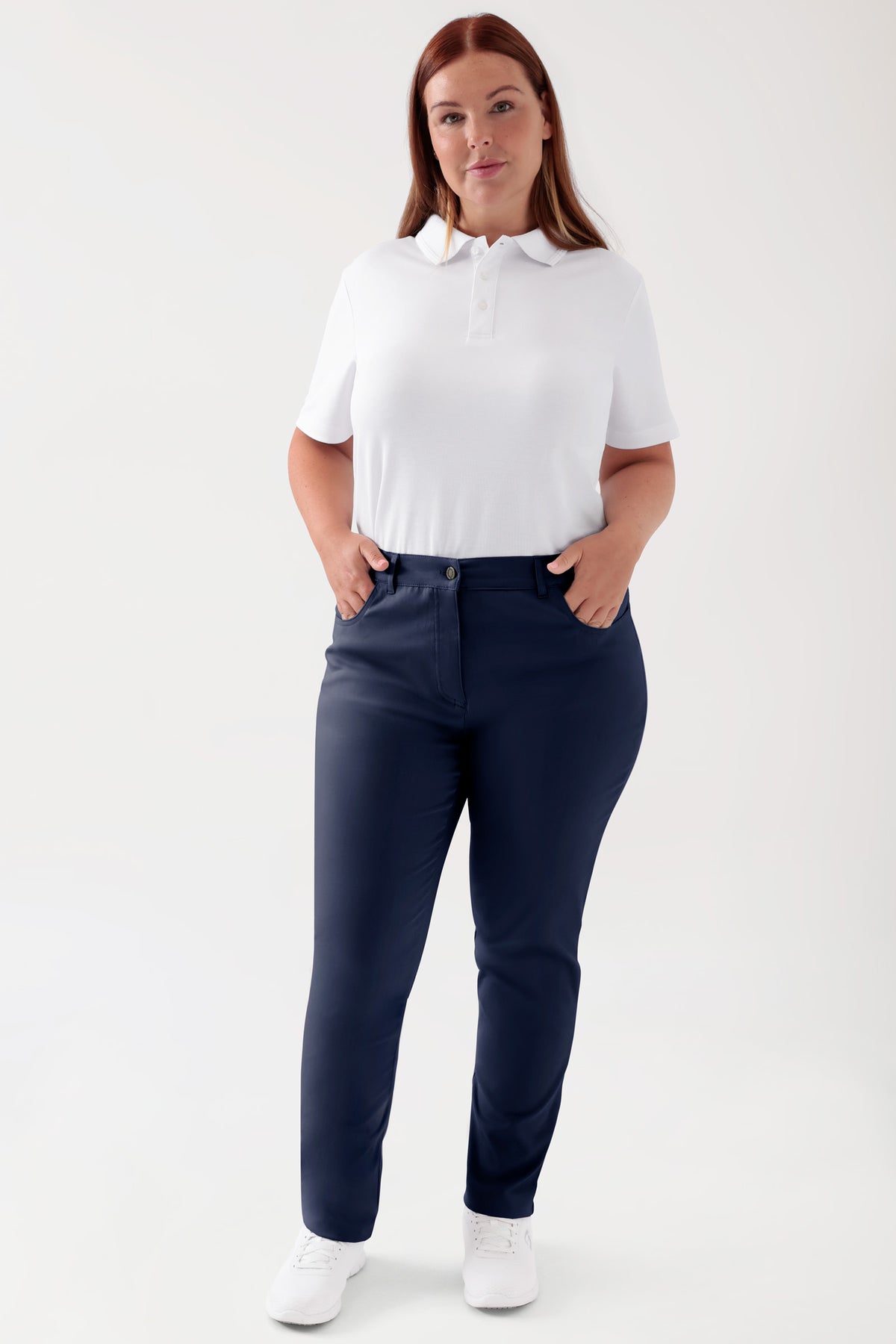 Frau in einem weißen Polohemd und einer COMFY FLEX 5-Pocket Hose Damen – schlankes Bein, navy mit hoher Taille und Komfort-Stretch, die ihre Hände in den Taschen hat., Vorderansicht Das Model ist 173 cm groß und trägt Größe 46