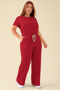 Frau, die eine rote KAERE-Hose für Damen – weites Bein, rot – mit einem kurzärmeligen Oberteil trägt; die Hose verfügt über einen bequemen Kordelzug in der Taille und eine lockere Passform mit weitem Bein.