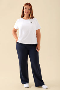 Eine Frau, die ein weißes KAERE-Shirt für Damen – Rundhalsausschnitt, weiß – mit einer Brusttasche und eine dunkelblaue Hose trägt.