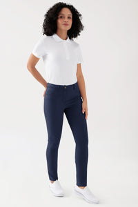 Eine Person, die ein weißes Poloshirt, eine COMFY FLEX 5-Pocket Hose Damen – schlankes Bein in Marineblau mit hoher Taille sowie weiße Sneaker trägt.