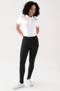 Eine Frau trägt ein weißes Poloshirt, weiße Sneaker und eine schwarze Hose COMFY FLEX 5-Pocket Hose Damen – schlankes Bein schwarz mit hoher Taille und schmaler Passform.