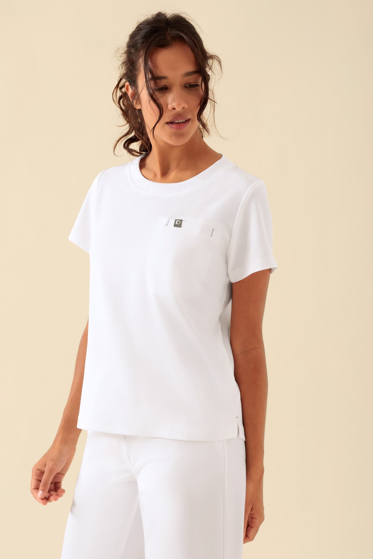 Eine Person trägt ein weißes, kurzärmeliges KAERE-Shirt für Damen – Rundhalsausschnitt, weiß, mit Rundhalsausschnitt und einer Brusttasche., Vorderansicht Das Model ist 176 cm groß und trägt Größe S
