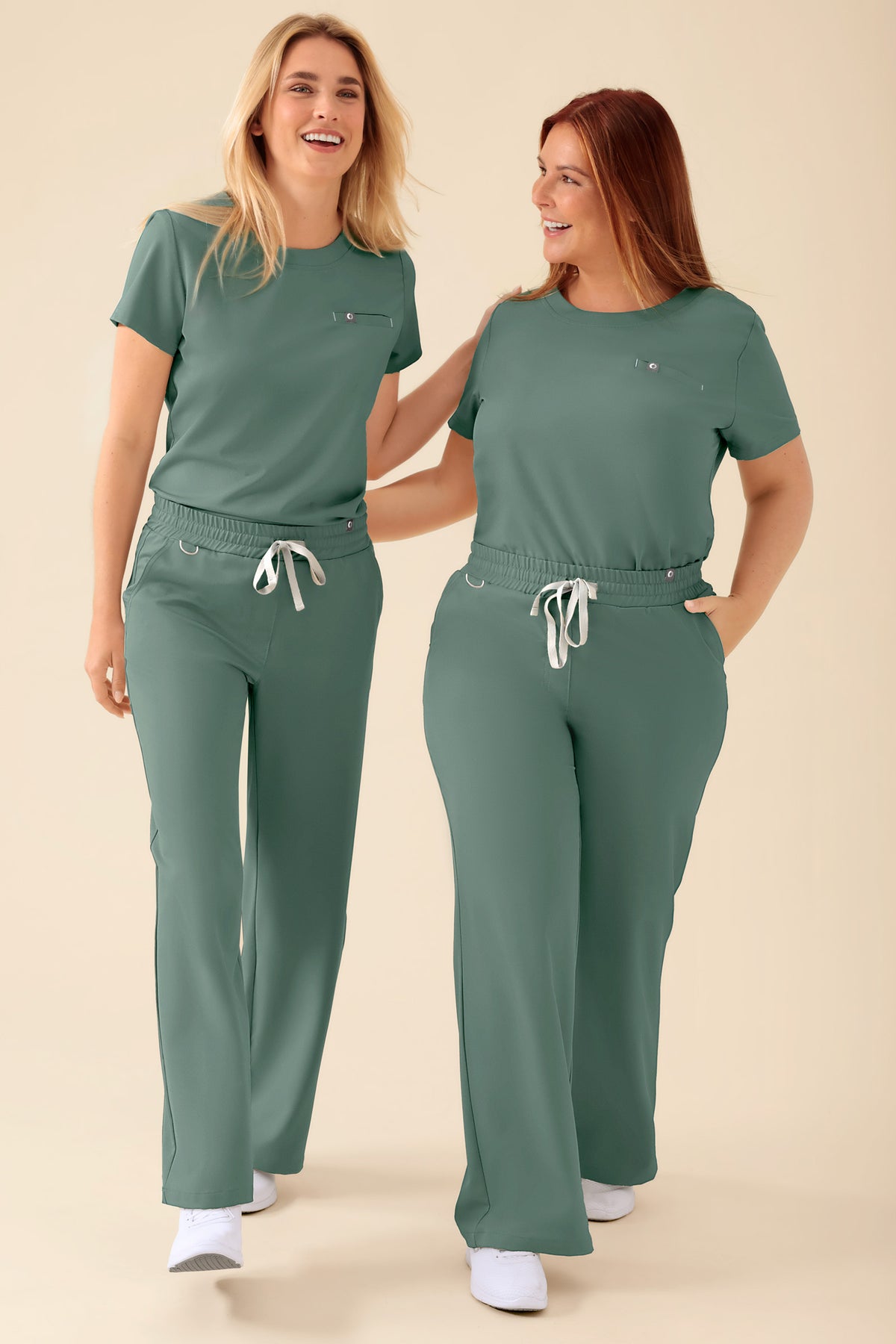 Zwei Frauen, die identische dunkelgrüne KAERE-Obershirts für Damen – Rundhalsausschnitt, dunkelgrün – sowie Hosen mit Kordelzug trugen., Vorderansicht