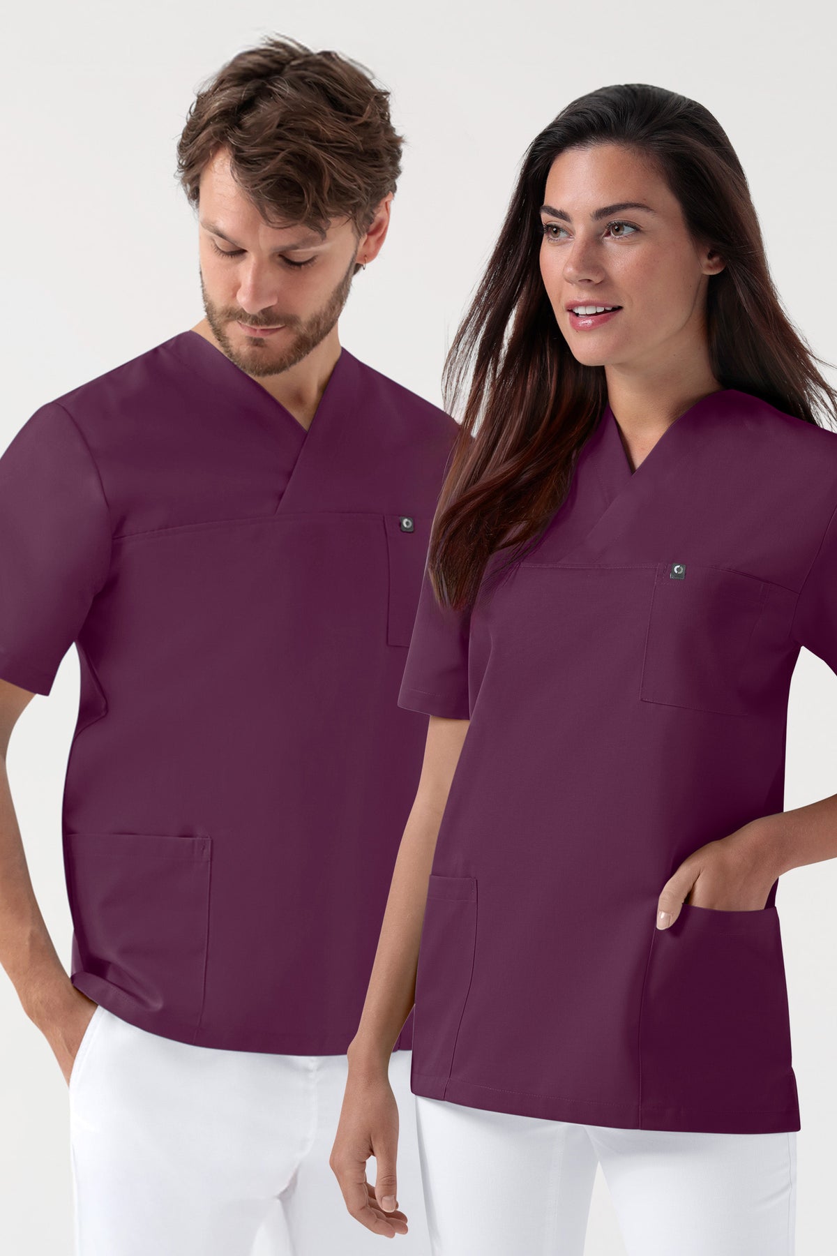 Ein Mann und eine Frau tragen passende, pflaumenfarbene GREEN Stretch Schlupfkasack Unisex - V-Ausschnitt pflaume-Kitteloberteile mit V-Ausschnitt und Brusttasche.