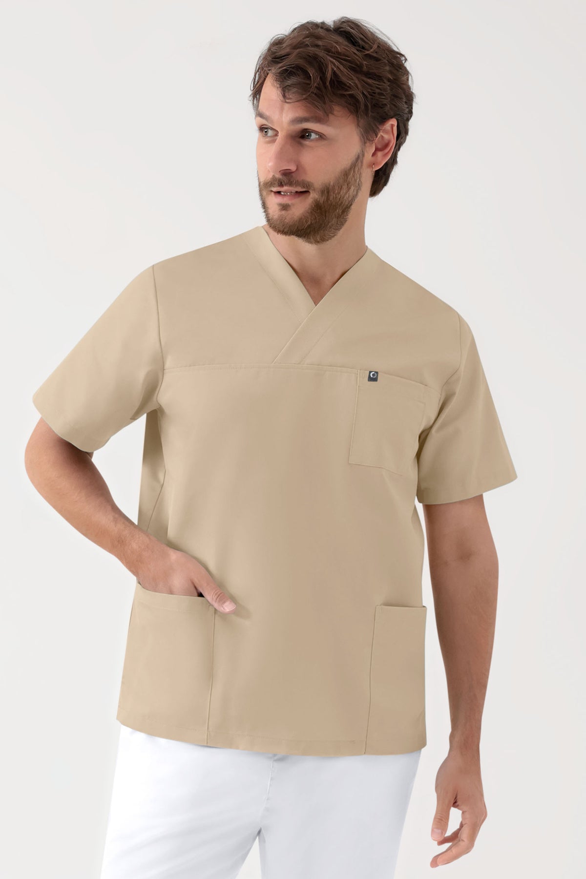Ein Mann, der einen CLINIC DRESS GREEN Stretch Schlupfkasack Unisex – V-Ausschnitt, sandfarben trägt, der über eine Brusttasche und zwei Seitentaschen verfügt., Vorderansicht