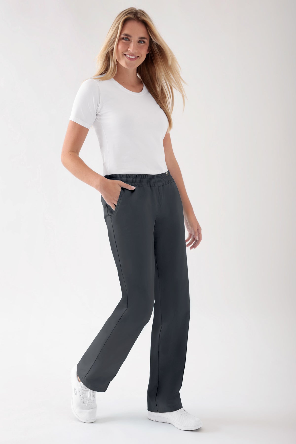Eine Frau trägt ein weißes T-Shirt und eine Hose von JUST STRONG Hose Damen – Gummibund anthrazit, die sich durch einen bequemen elastischen Bund und praktische Seitentaschen auszeichnet.