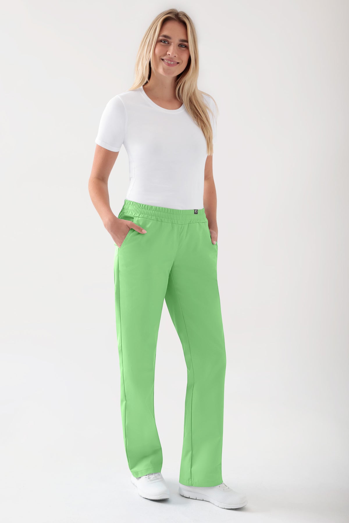Eine Person, die ein weißes T-Shirt und eine apfelgrüne JUST STRONG Hose Damen – Gummibund apfelgrün mit geradem Bein trägt, eine OP-Hose mit rundem Gummibund und Kordelzug.