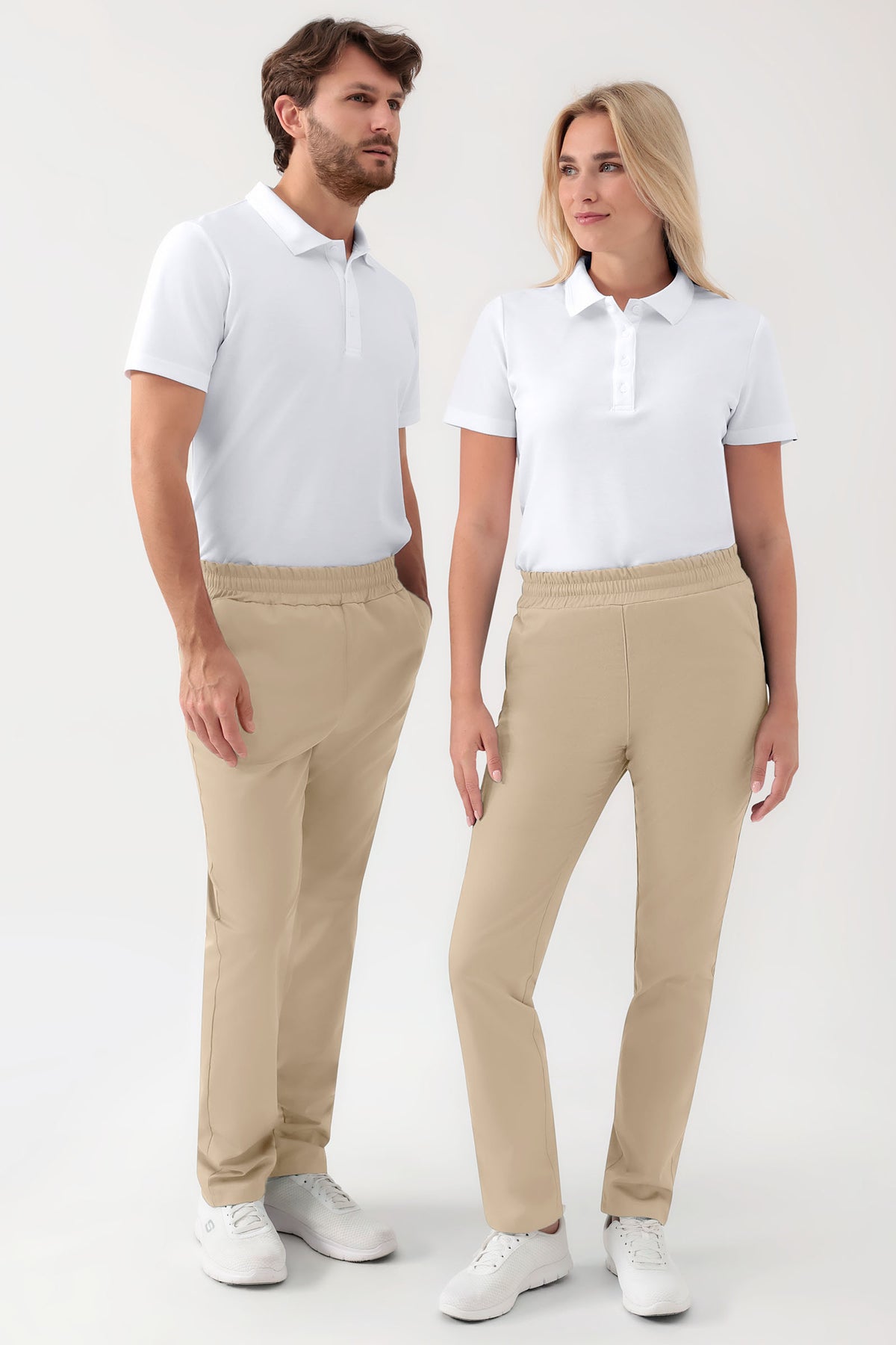 Ein Mann und eine Frau tragen weiße Poloshirts und GRÜNE Stretch-Hosen Unisex – Rundumgummibund in Sand, die über einen bequemen elastischen Bund und ein lässiges, weit geschnittenes Hosenbein verfügen.