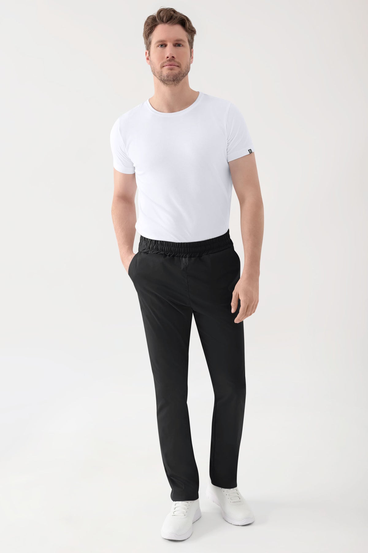 Ein Mann, der ein weißes T-Shirt und eine schwarze Unisex-Hose Stretch Hose mit lockerer Passform und elastischem Bund trägt.