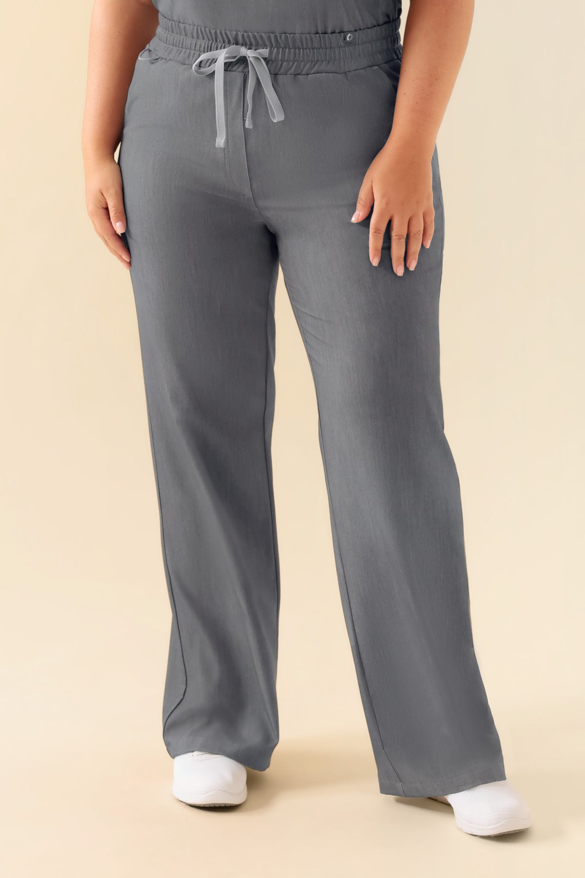 KAERE Hose Damen – weit geschnittene Scrub-Hose in Grau meliert mit bequemem elastischem Bund und Kordelzug, kombiniert mit weißen Schuhen., Vorderansicht