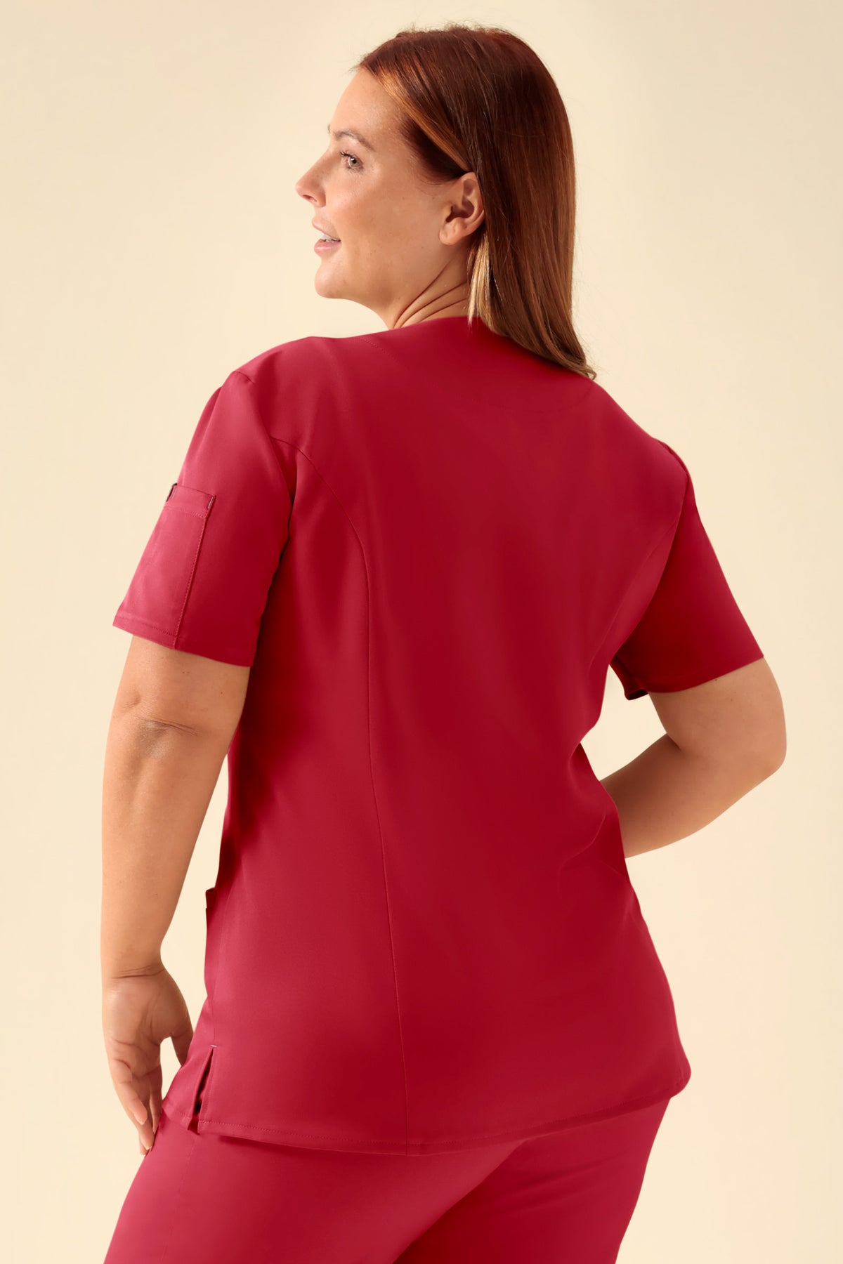 Eine Frau, von hinten gesehen, die ein rotes KAERE Kasack Damen – durchgeknöpftes rotes OP-Oberteil mit V-Ausschnitt und eine dazu passende Hose mit Seitentaschen trägt., Rückansicht Das Model ist 173 cm groß und trägt Größe XL