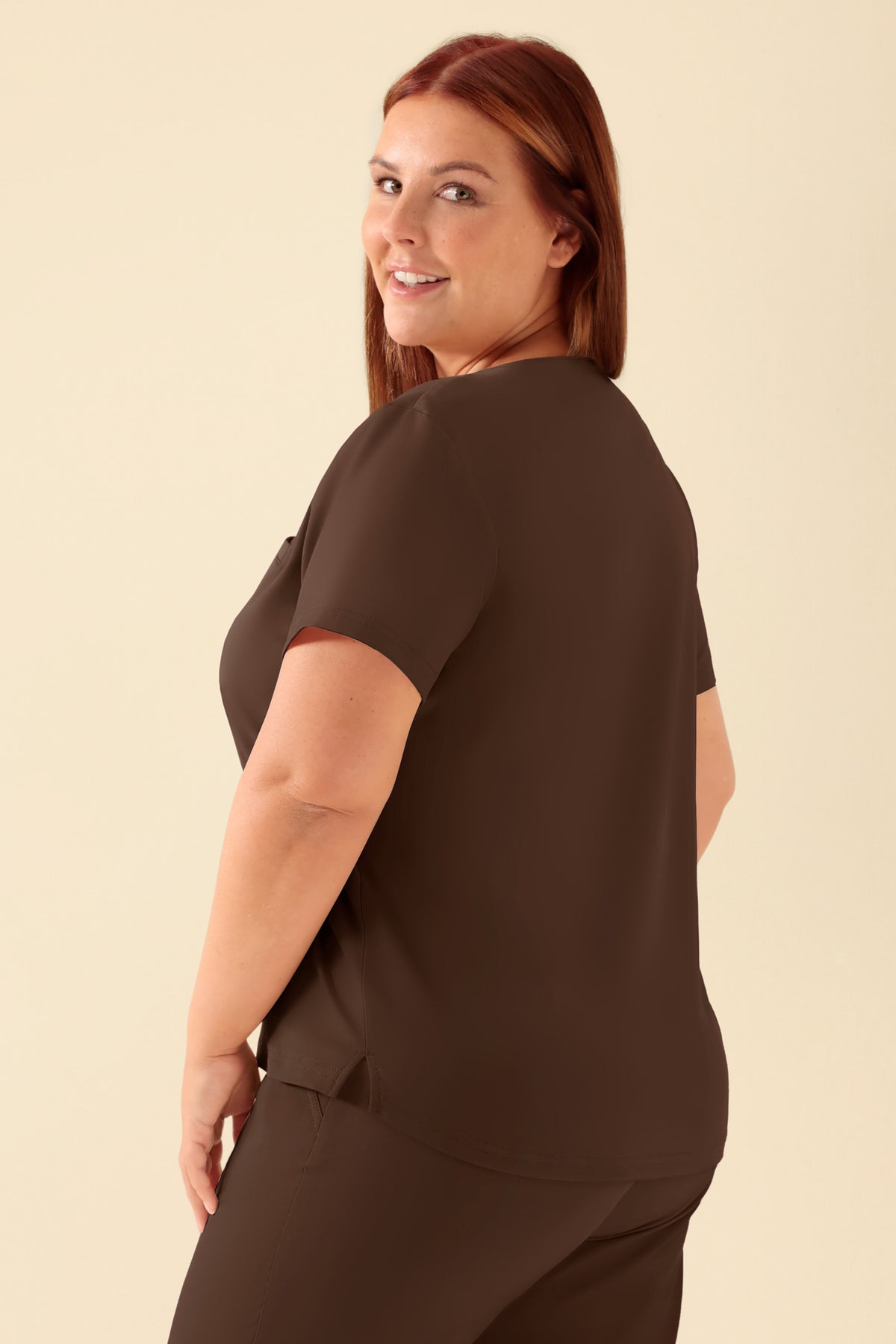 Eine Frau, die ein braunes KAERE-Shirt für Damen – Rundhalsausschnitt in der Farbe Coffee mit Rundhalsausschnitt und Brusttasche trägt., Rückansicht Das Model ist 173 cm groß und trägt Größe XL