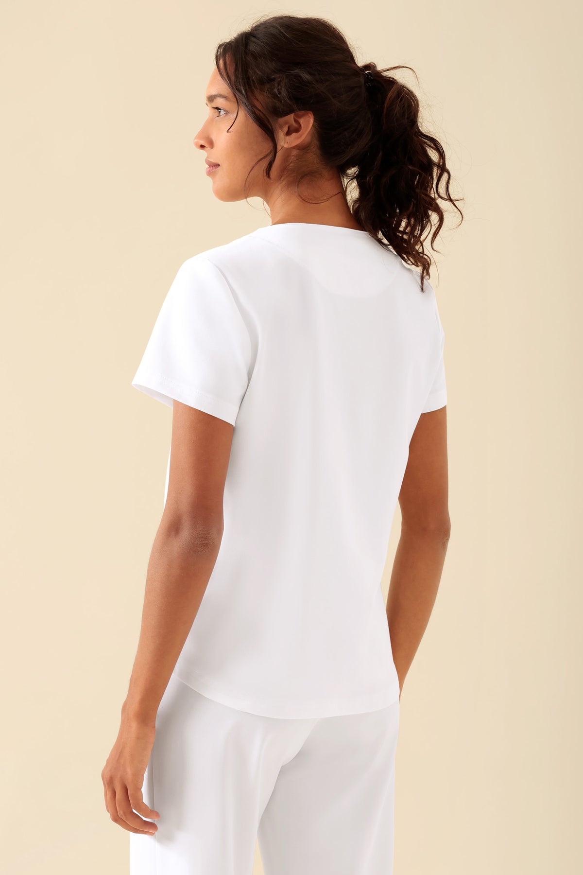 Rückansicht einer Frau, die ein weißes KAERE-Shirt für Damen mit Rundhalsausschnitt, kurzen Ärmeln und einer Brusttasche trägt., Rückansicht Das Model ist 176 cm groß und trägt Größe S