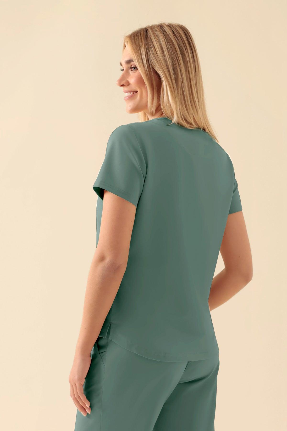 Eine Frau, von hinten gesehen, die ein dunkelgrünes KAERE Shirt Damen – Rundhalsausschnitt dunkelgrün mit Rundhalsausschnitt und einer einzelnen Brusttasche trägt., Rückansicht Das Model ist 177 cm groß und trägt Größe S
