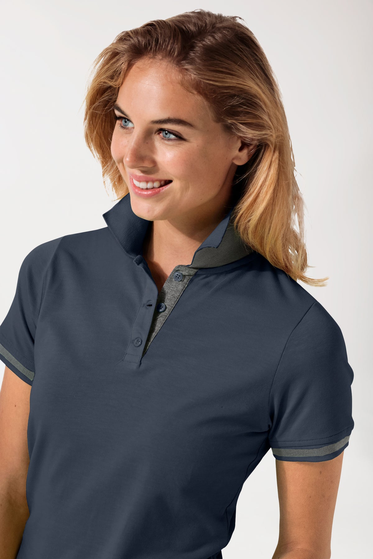 Eine Frau trägt ein CLINIC DRESS Stretch Shirt Damen – Polokragen navy/dunkelgrau melange, ein tailliertes, marineblaues Kurzarm-Poloshirt mit dunkelgrauem Kontrastkragen und kontrastfarbenen Ärmelbündchen.